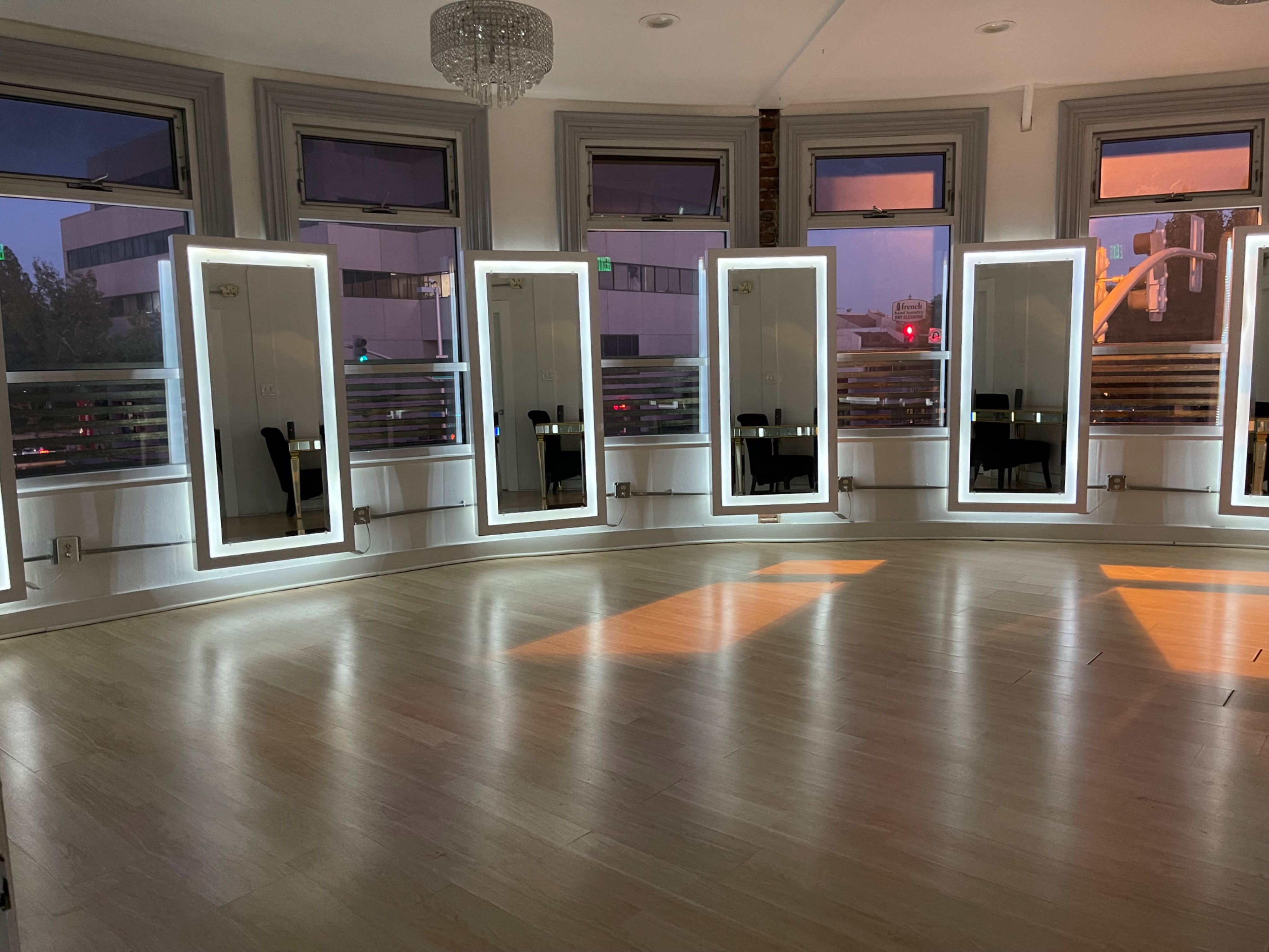 A yoga studio features a practice area with a mat and blocks arranged on the wooden floor, surrounded by large mirrors.