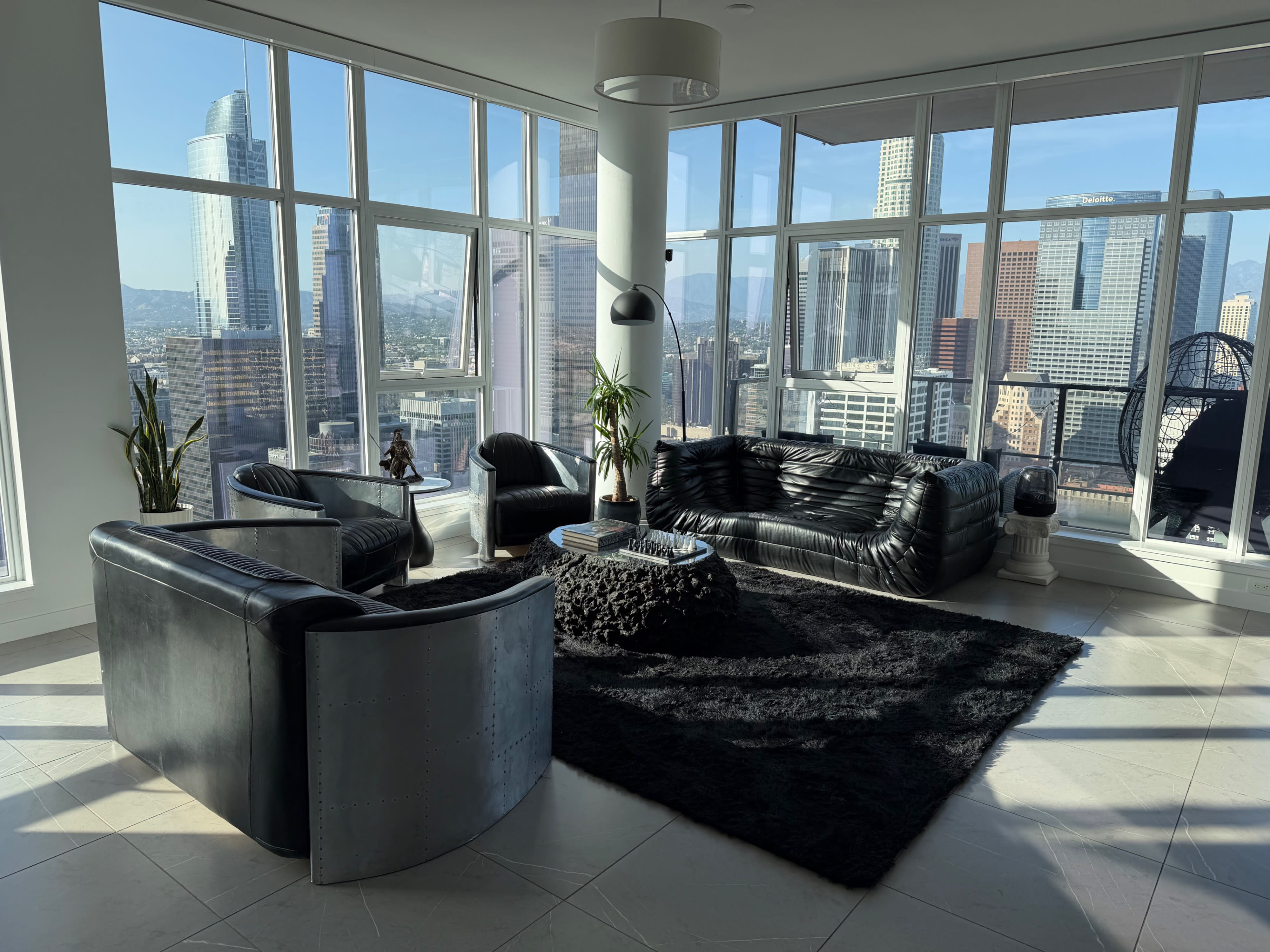 People are gathered at a birthday party on a high-rise balcony overlooking a city skyline at night, illuminated by purple lighting.