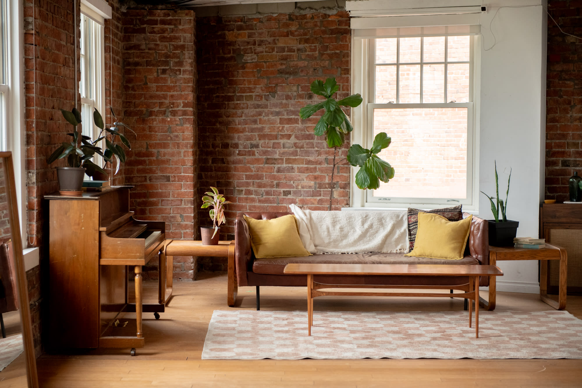 A person sits casually on a sofa in a relaxed indoor setting, resting one arm on the back and gazing thoughtfully out the window.
