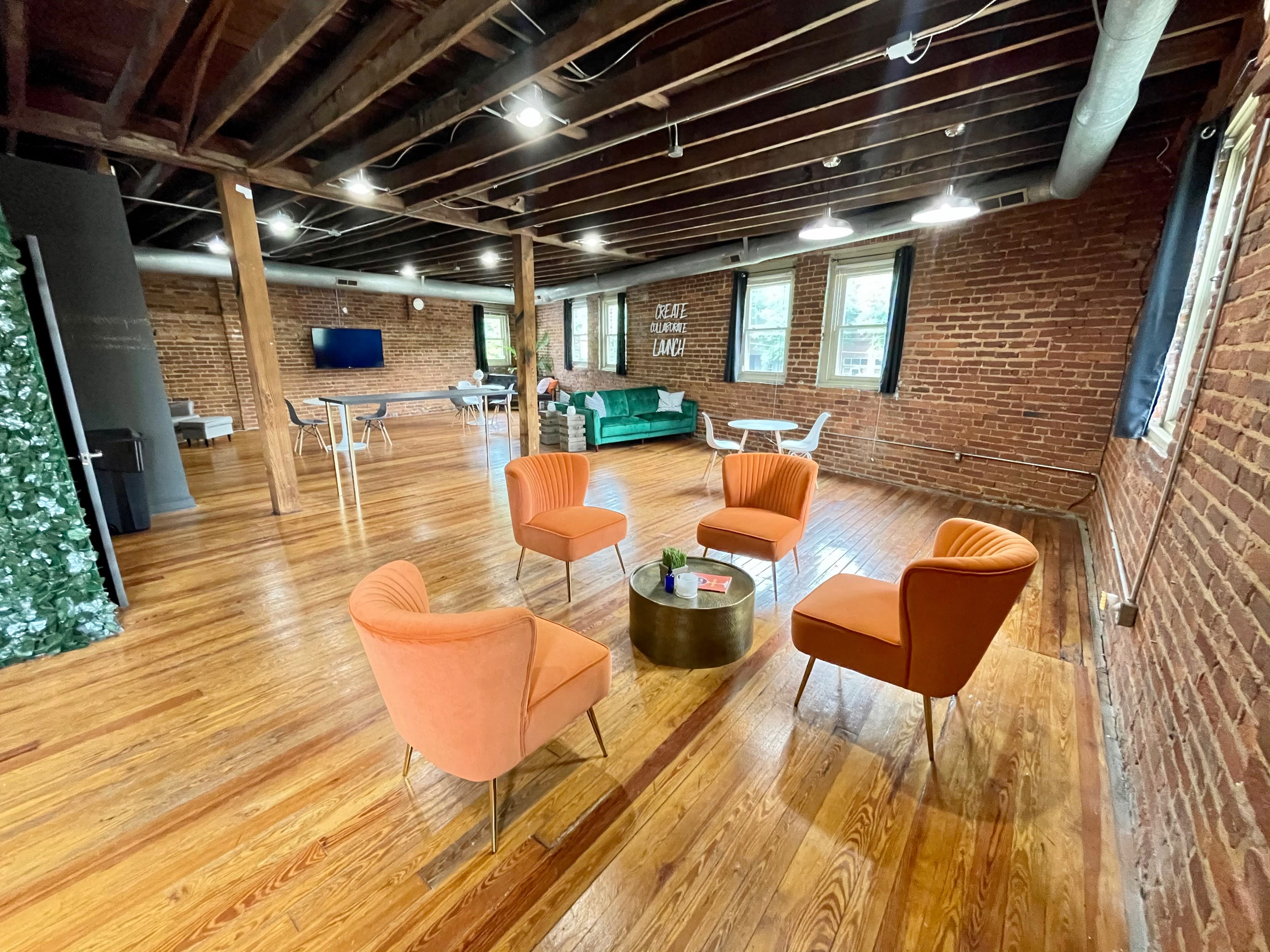 A private party is set up in a rustic space featuring green couches, floral arrangements, and a sign on the wall that reads "CREATE COLLABORATE LAUNCH."