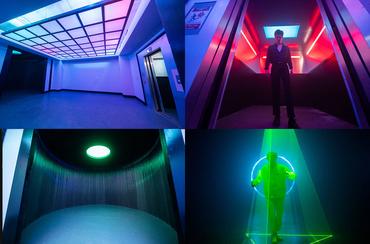 A performer stands in a dimly lit space surrounded by beams of laser light, creating a dramatic visual backdrop.