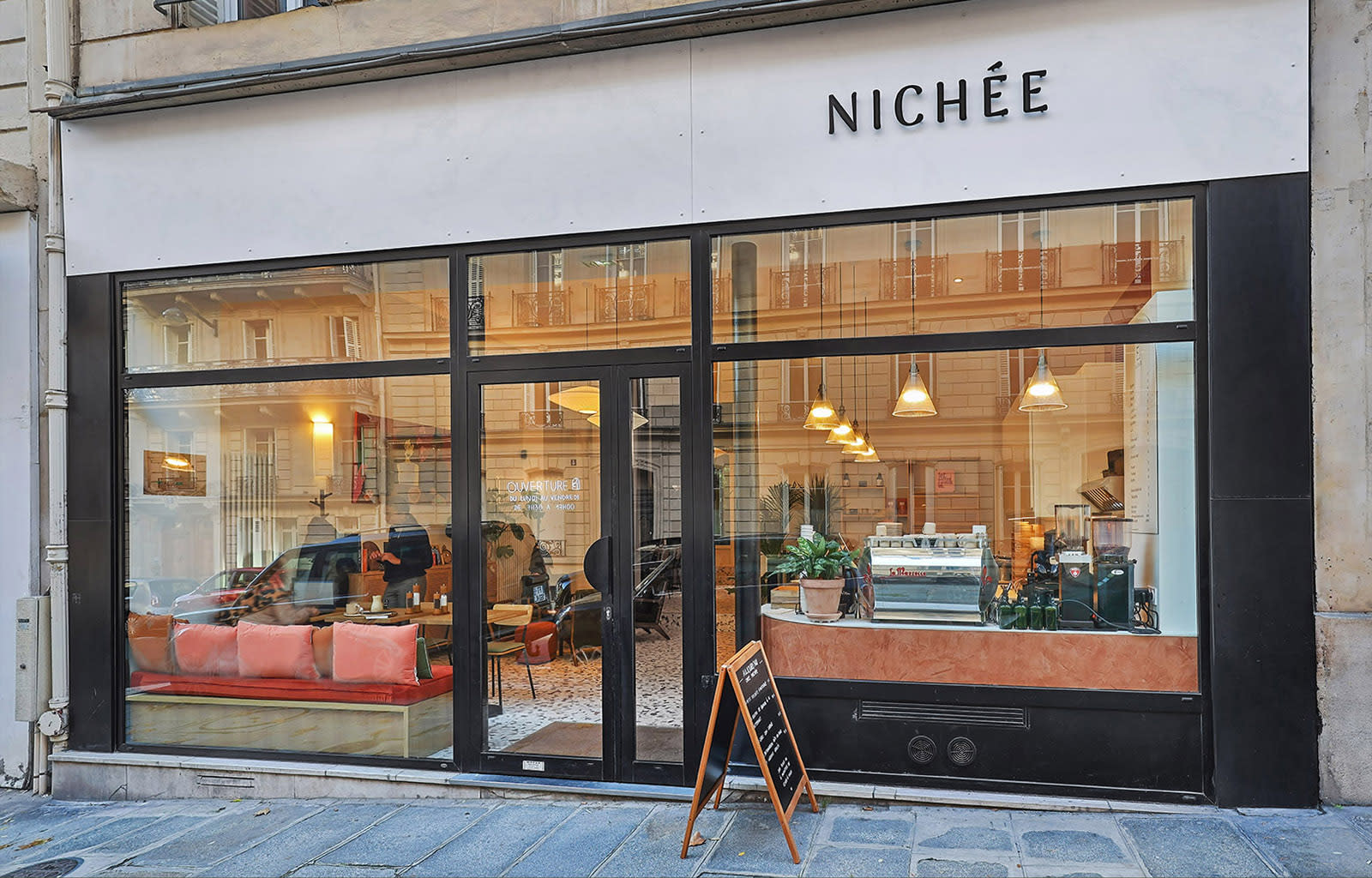 A cozy seating area featuring orange and green pillows overlooks a street with parked cars.