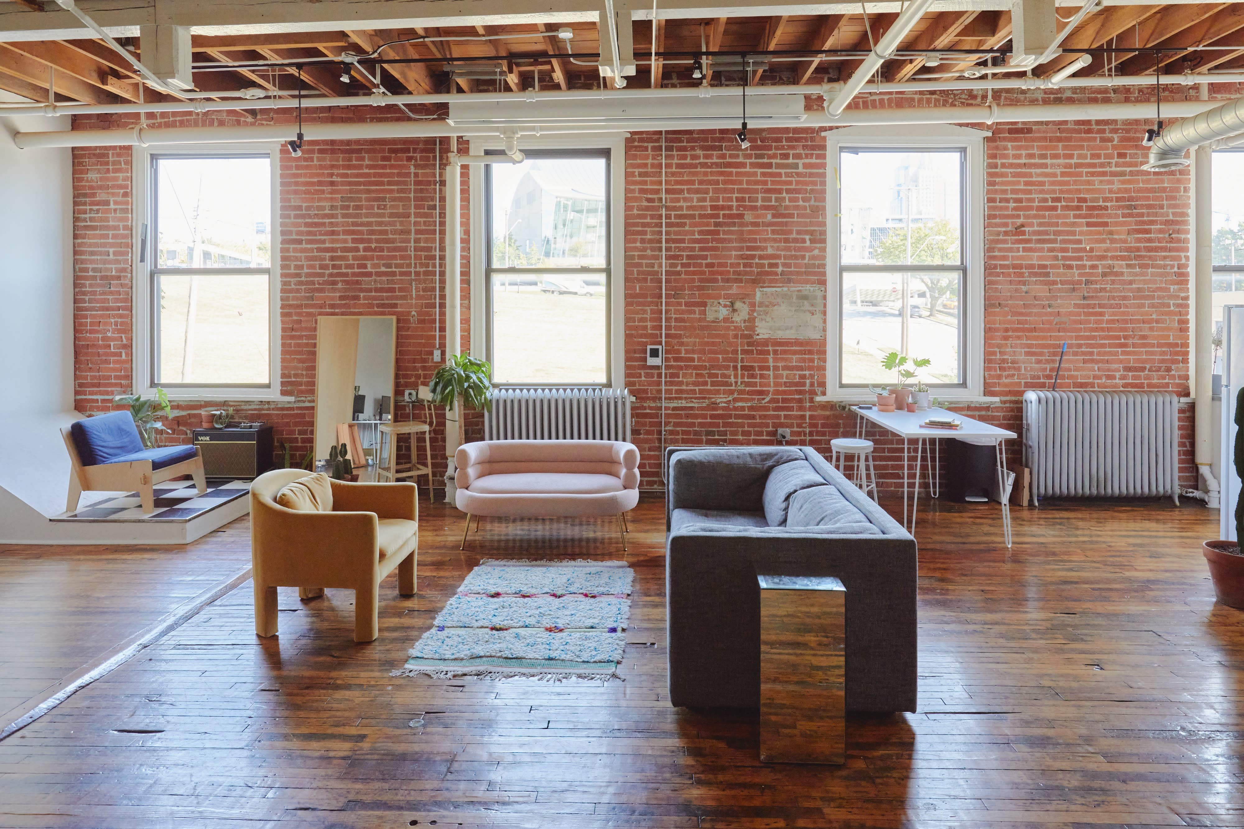 A person reclines on a pink sofa in a bright room with exposed brick walls, showcasing a casual photo shoot.