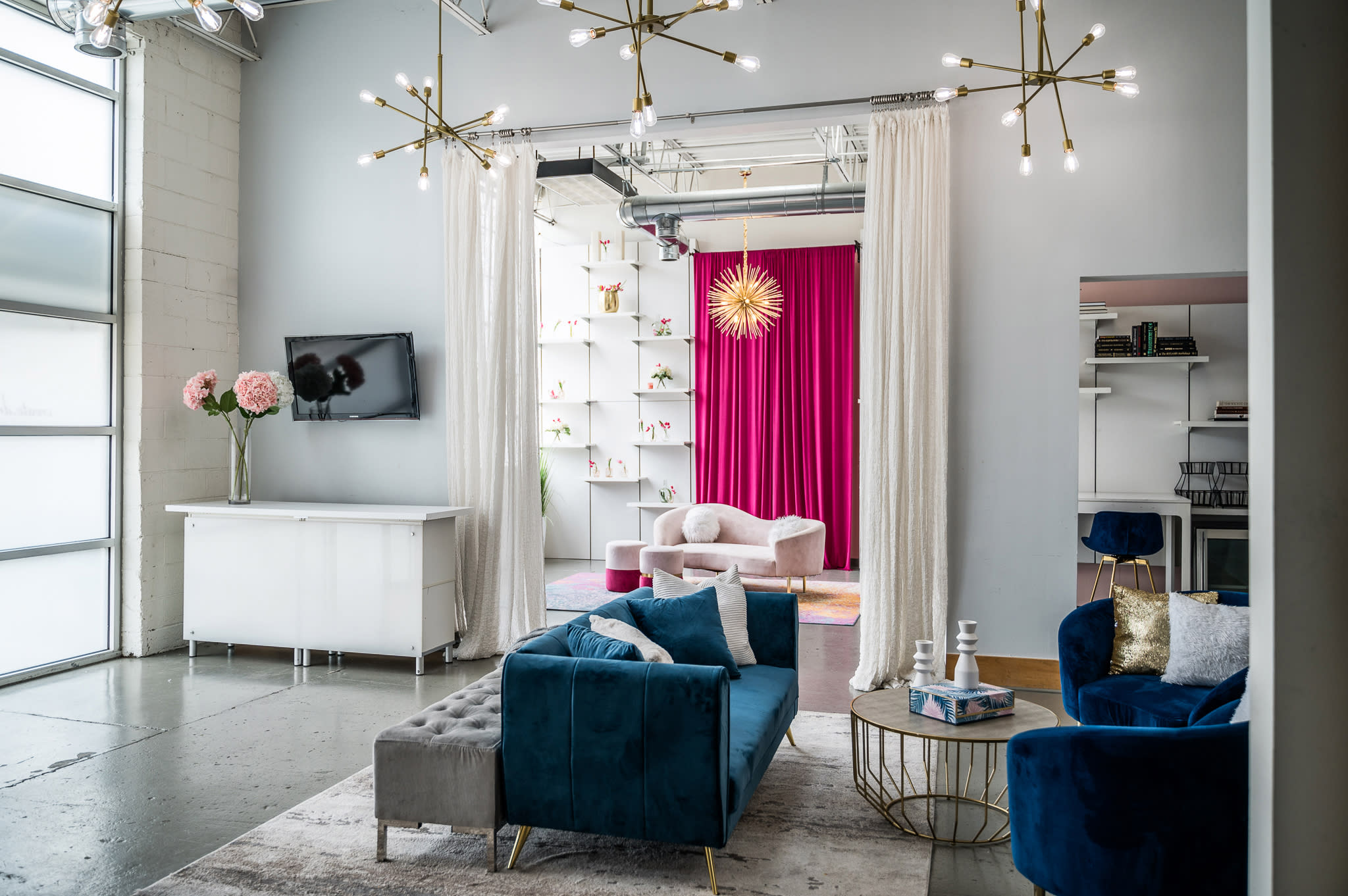 The scene features a festive birthday brunch setup with a pink curtain backdrop, decorative shelves, and a stylish seating arrangement.