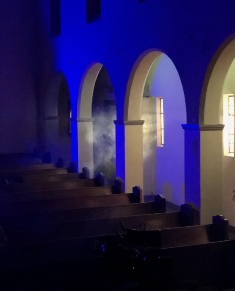 A crew films a dance music video featuring a solo performer seated on a church pew.