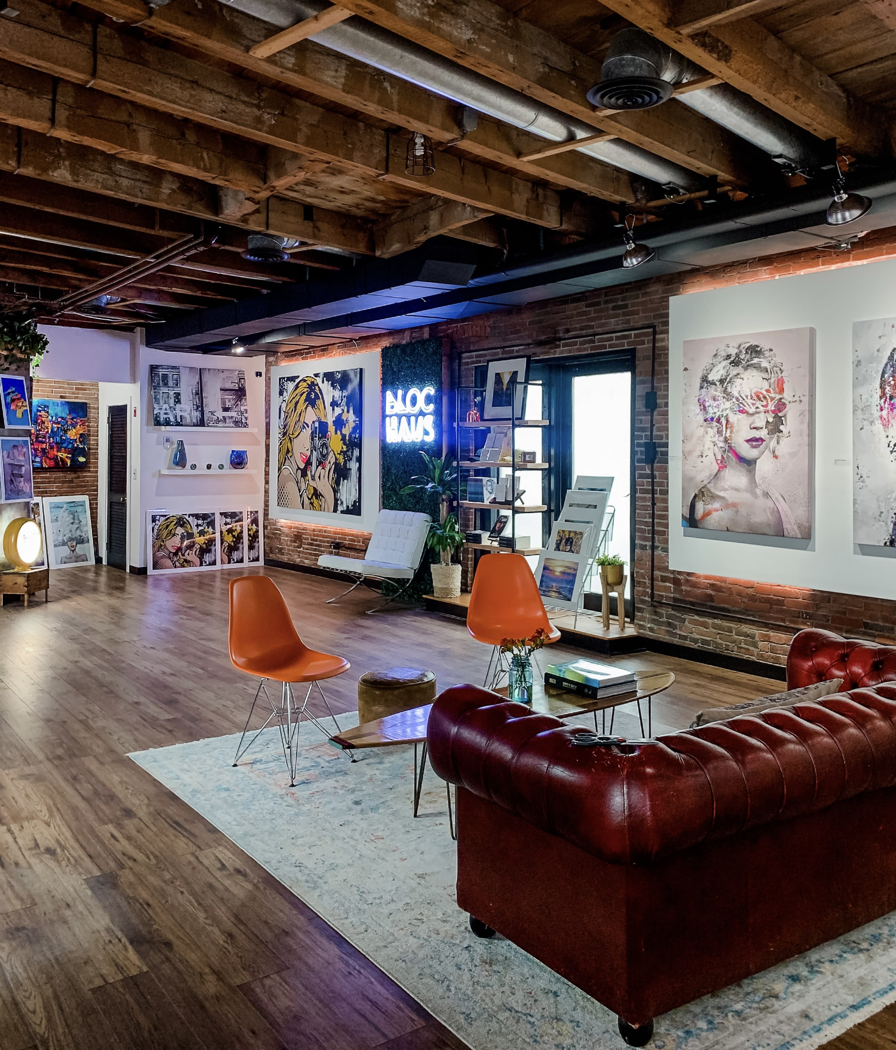 A man sits on a red leather couch during a video shoot in a creatively decorated indoor space.
