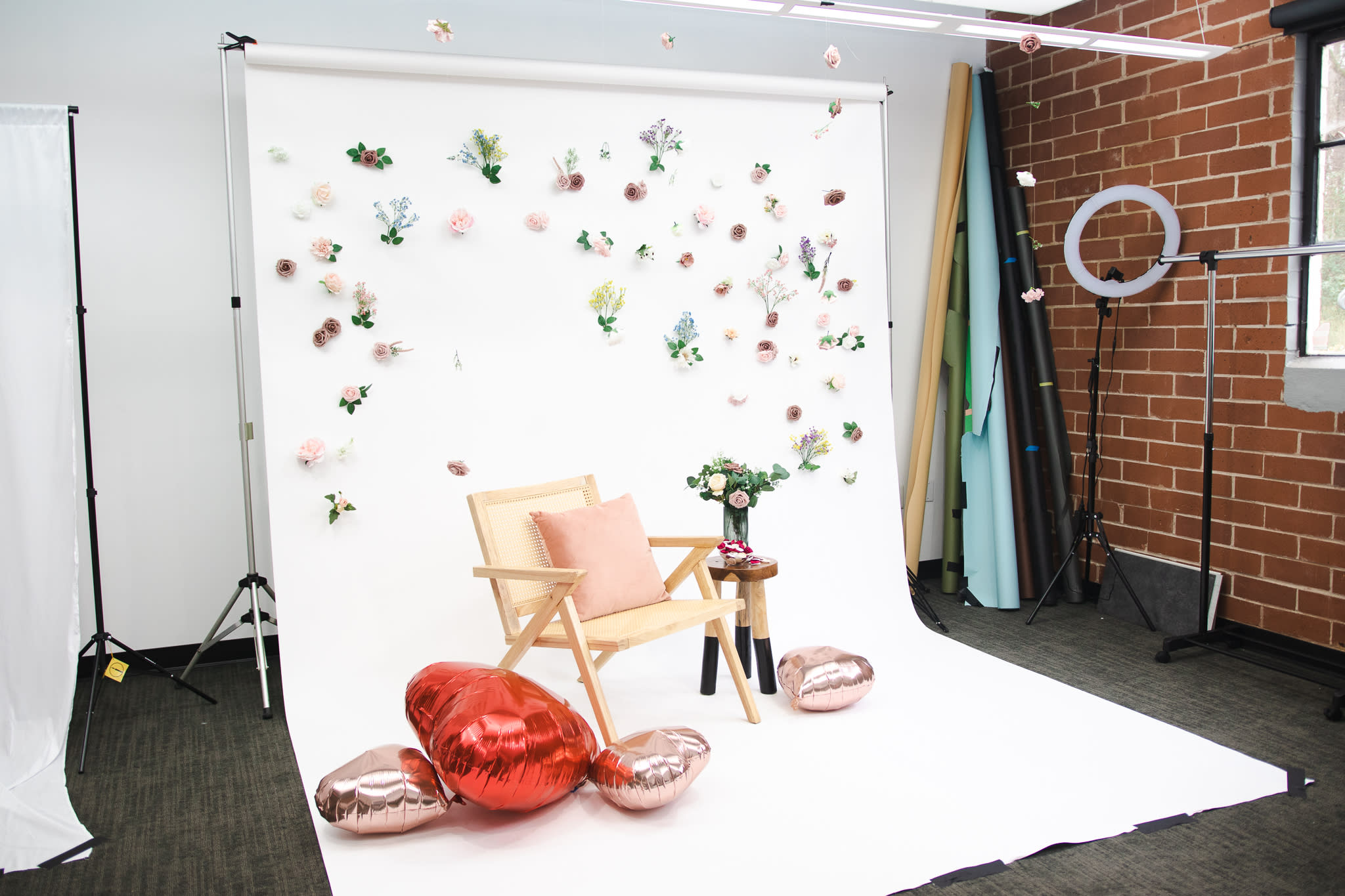 Two women sit back-to-back on a white backdrop decorated with floral arrangements, wearing matching tie-dye loungewear during a video shoot.