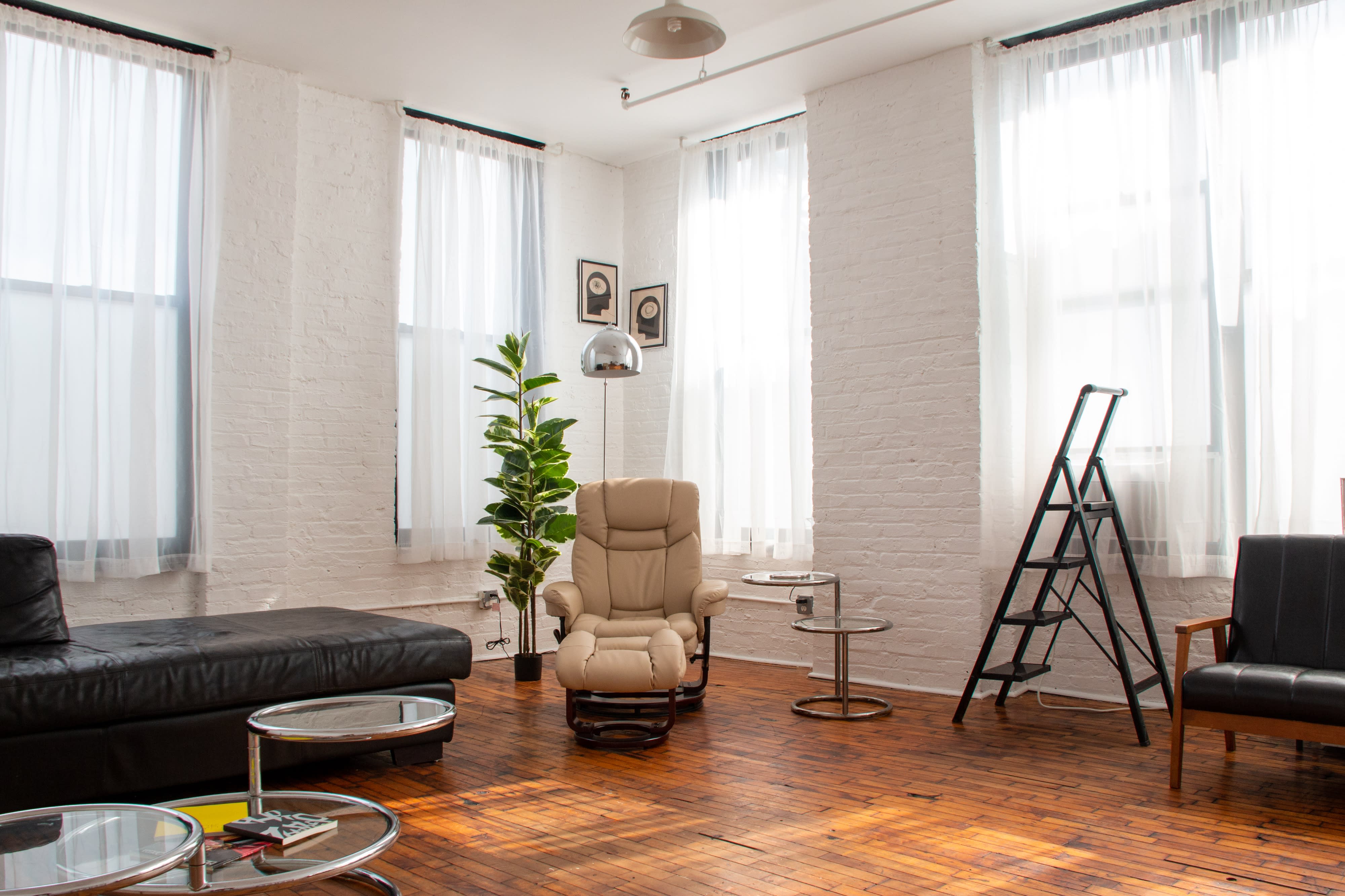 A photographer sets up for a photo shoot in a spacious, sunlit studio featuring large windows and minimalist decor.