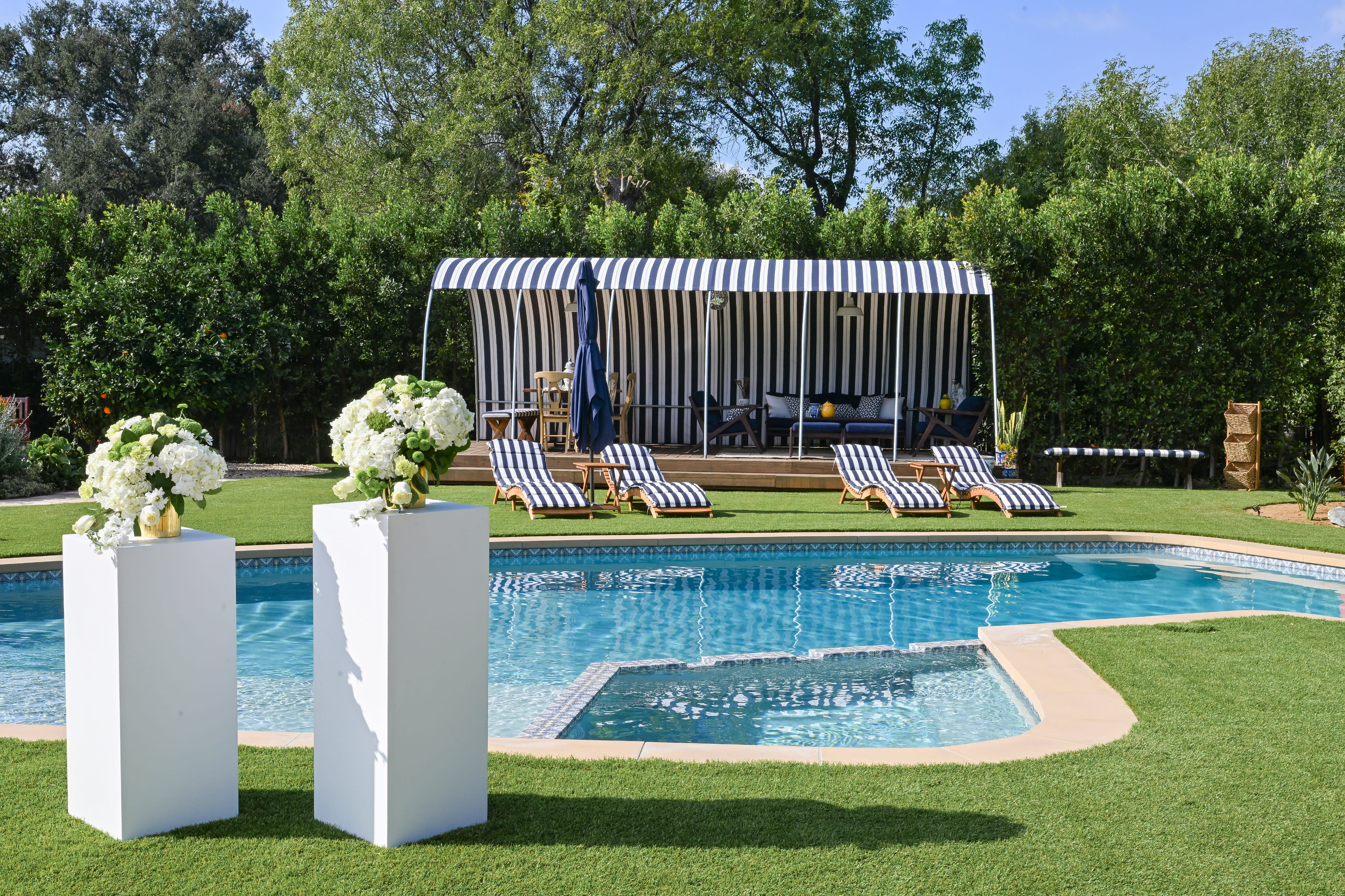 A woman lounges on a striped chaise, relaxing by a pool while wearing a bikini and a wide-brimmed hat.
