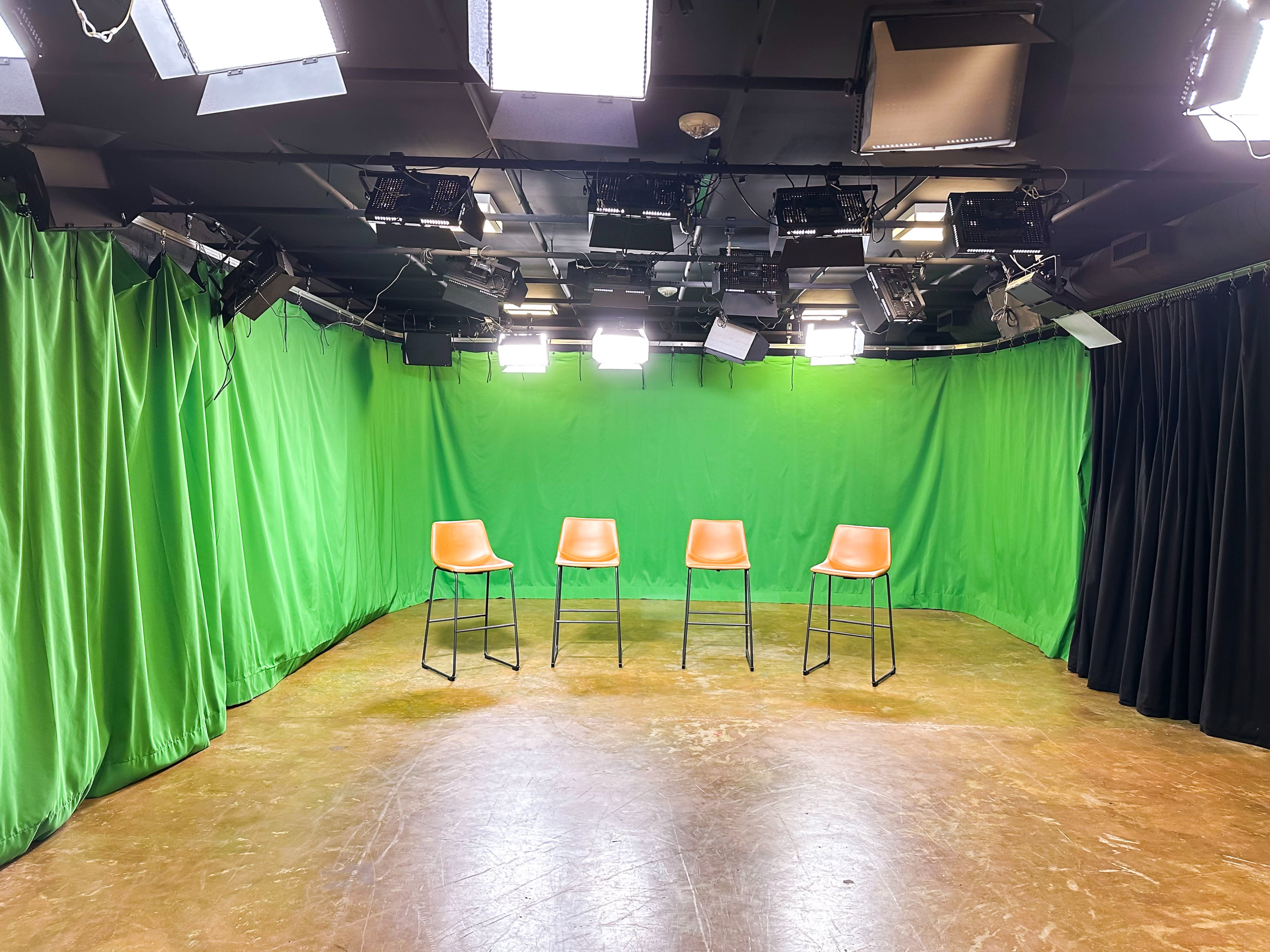 A man holds a card while a woman films him with a camera set up under a bright light during a video shoot.