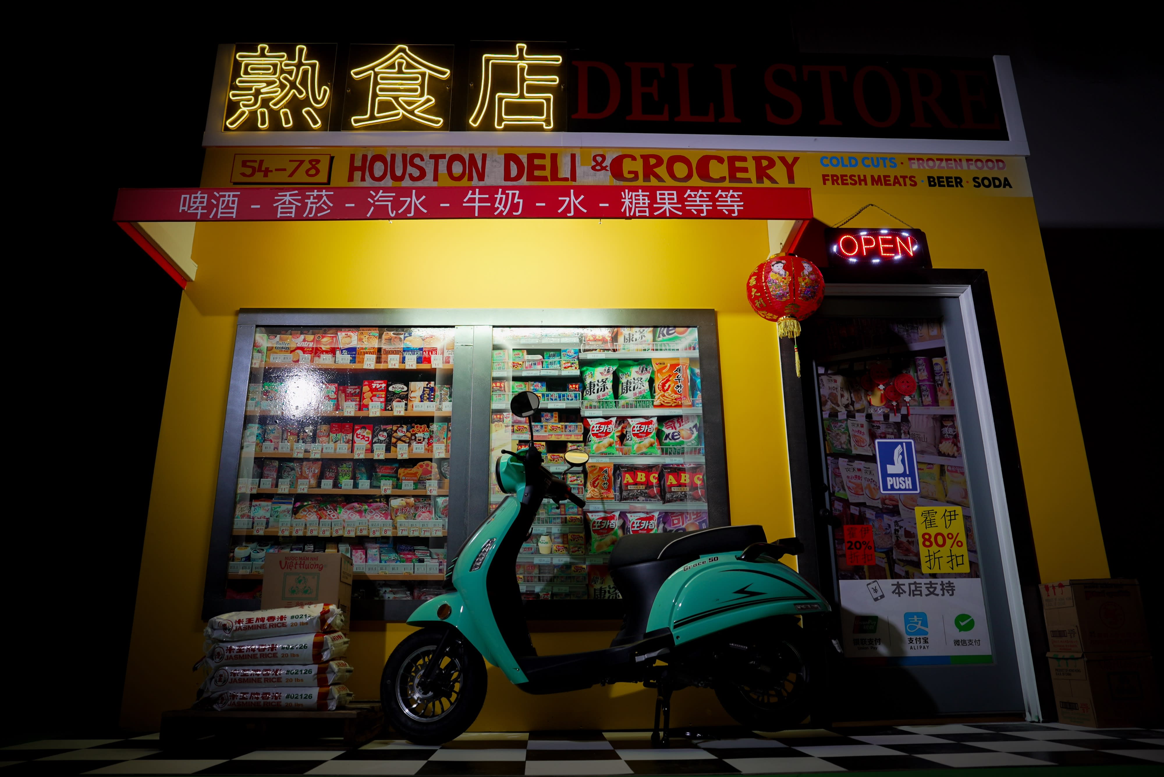 A person poses in a vibrant yellow outfit in front of a colorful grocery store, celebrating their birthday during a photo shoot.