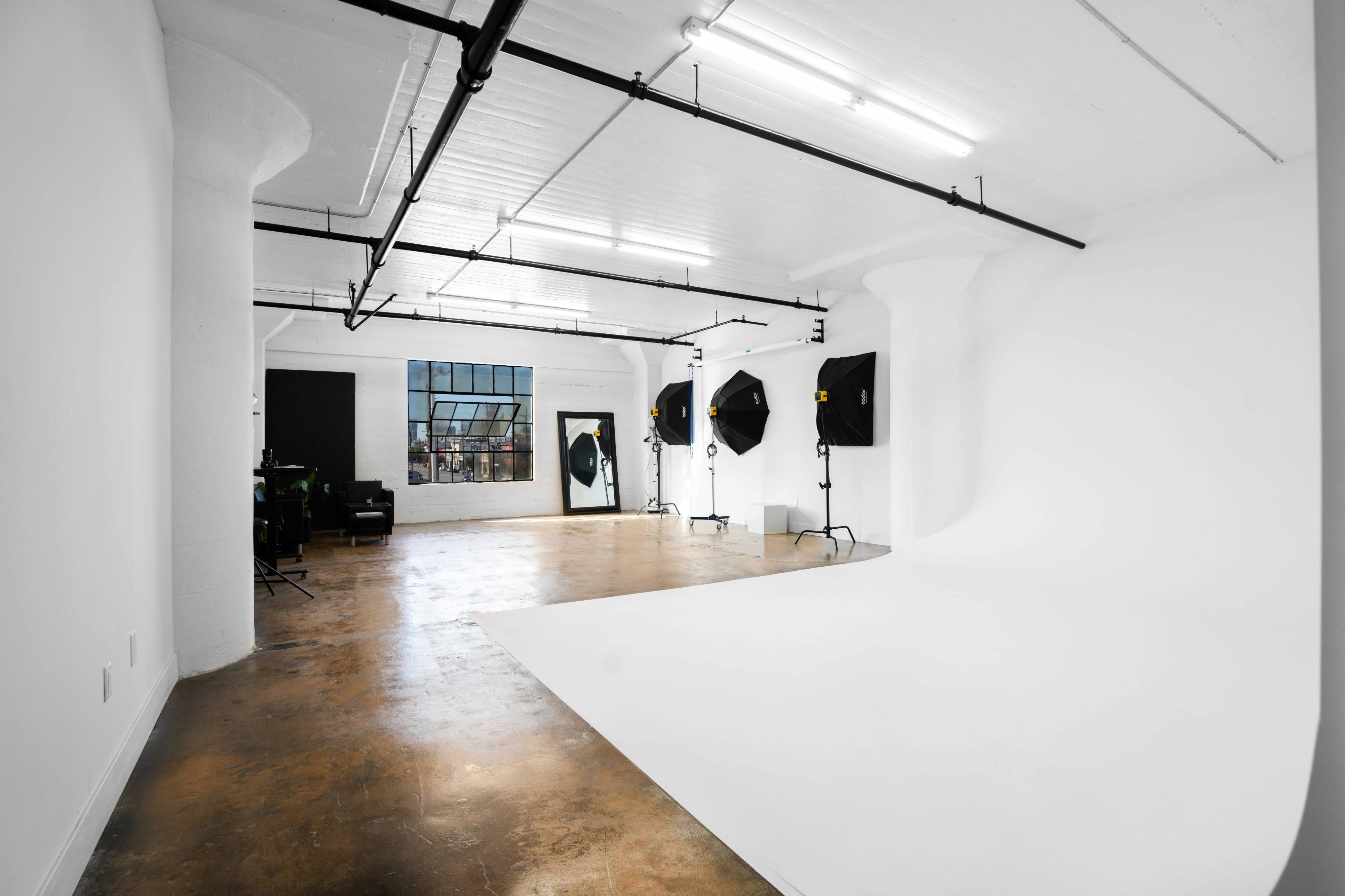 A person stands in front of a white backdrop during a film shoot, while a camera and equipment capture the scene.