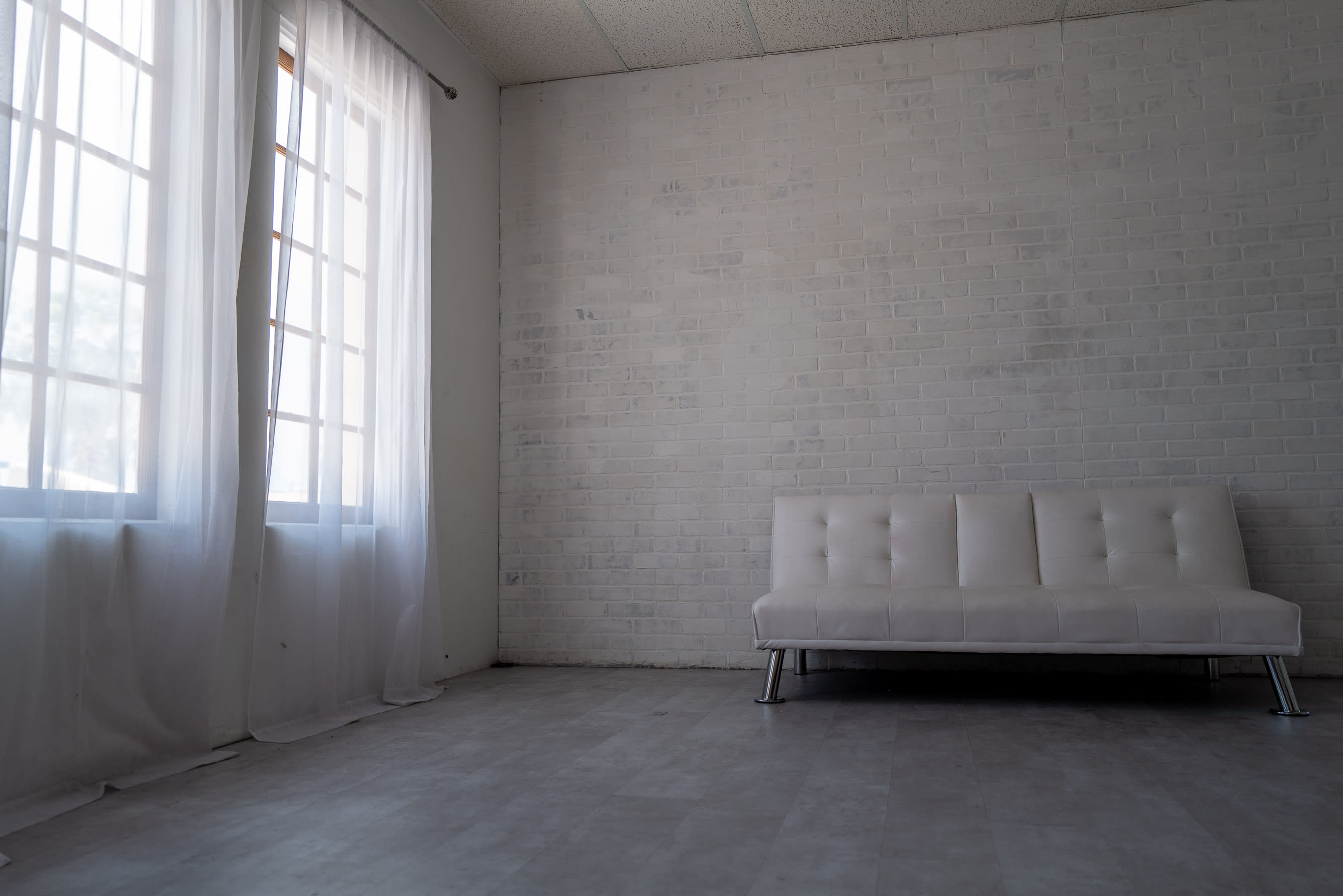 A model poses in a black swimsuit and transparent ballet slippers while sitting on the floor, draped in a red robe against a white brick wall.