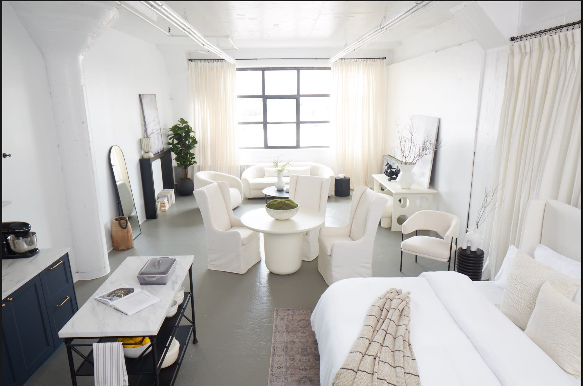 A photoshoot is taking place in a modern, minimalist living room featuring light-colored furniture and large windows overlooking an urban skyline.