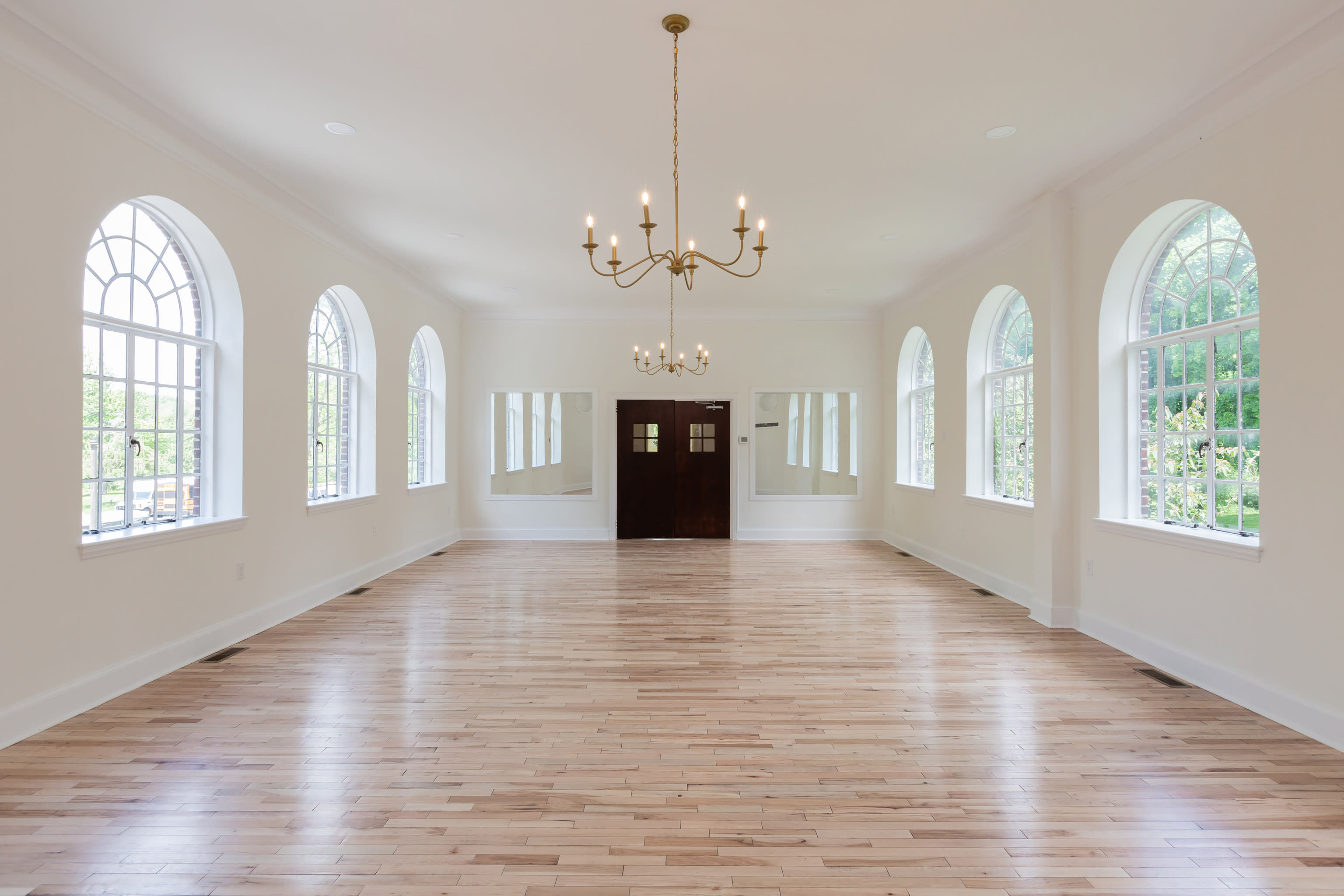 A wedding ceremony setup features white chairs arranged in rows facing a wooden door adorned with floral arrangements and a petal-strewn walkway.
