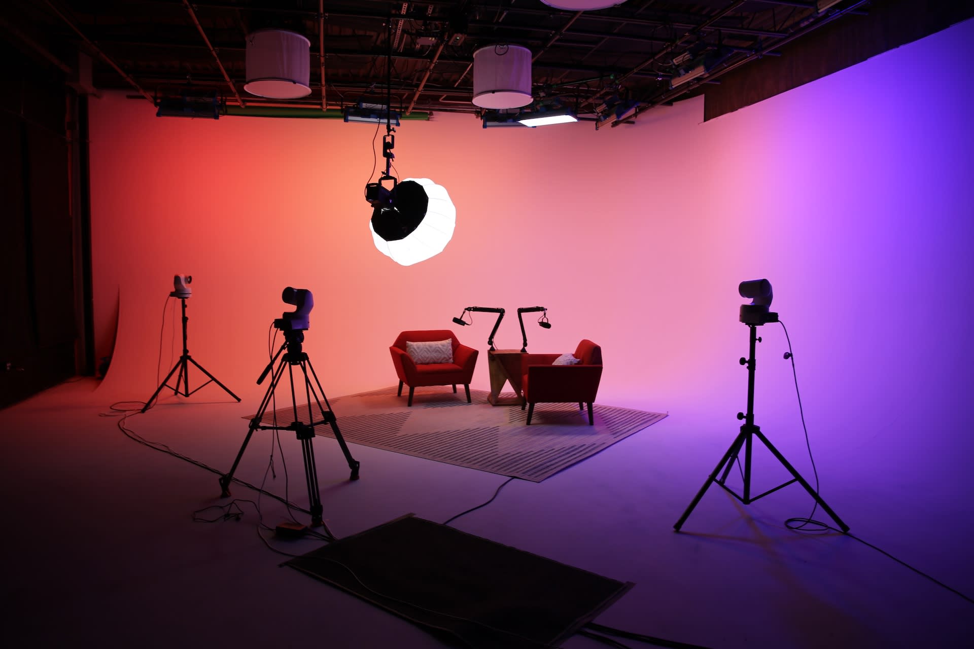 The image depicts a brightly lit studio setup for a videography shoot, featuring a green sofa, a wooden table, decorative plants, and various props arranged against a colorful backdrop.