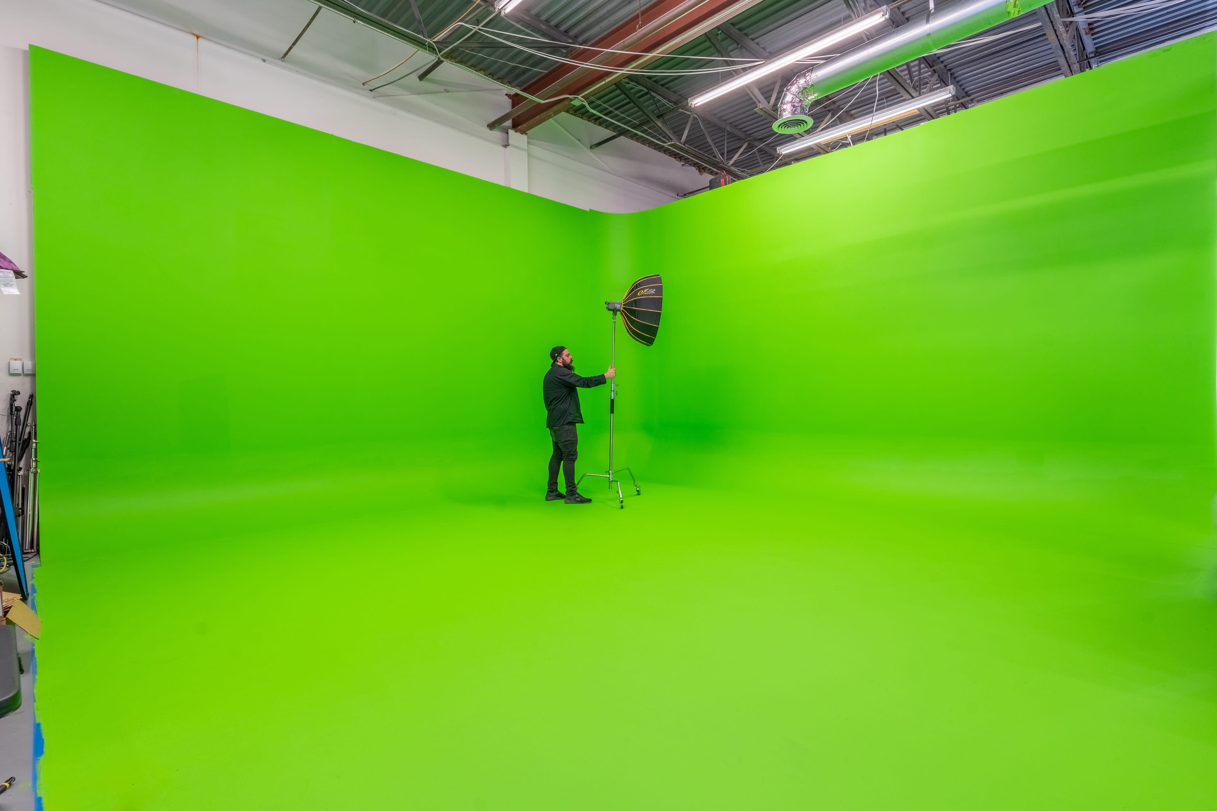 A person in a white outfit and goggles performs in front of a camera on a green screen set.