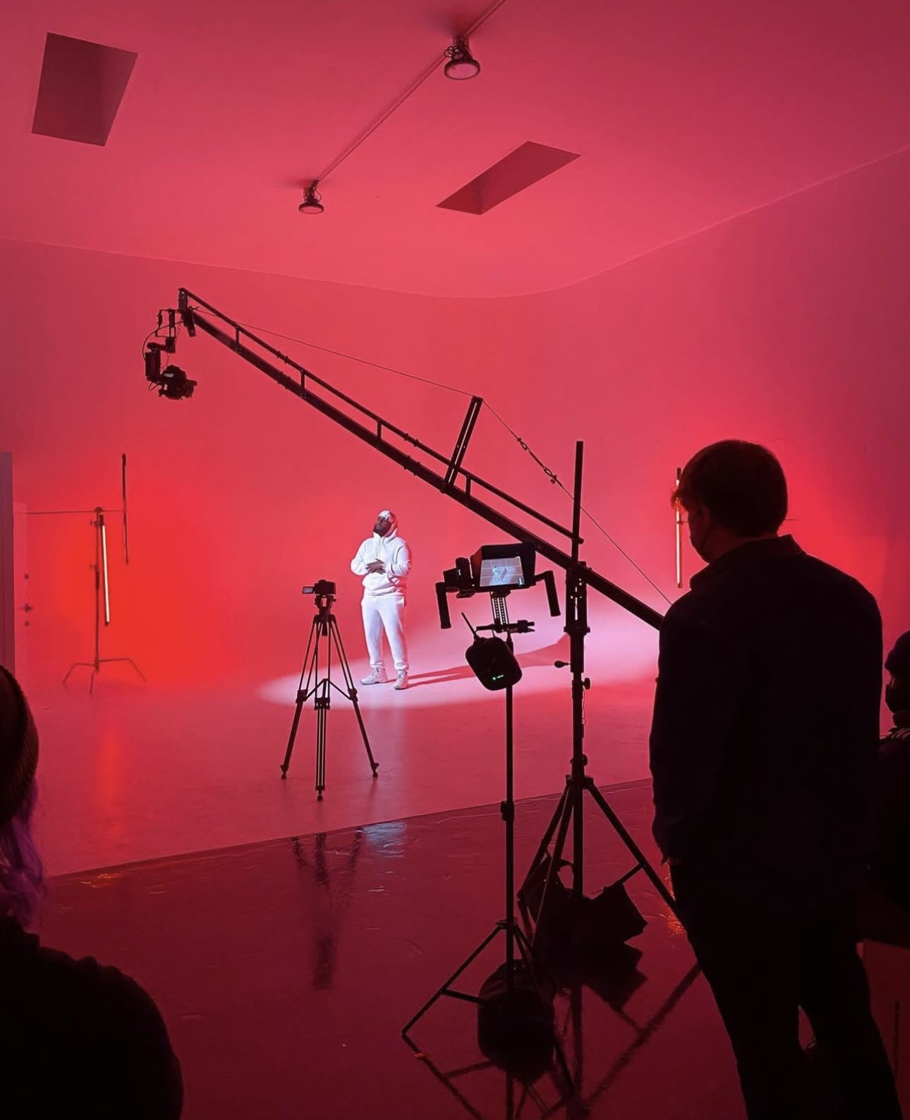 A photoshoot is taking place in a minimalistic studio setting with a subject posing on a chair under professional lighting.
