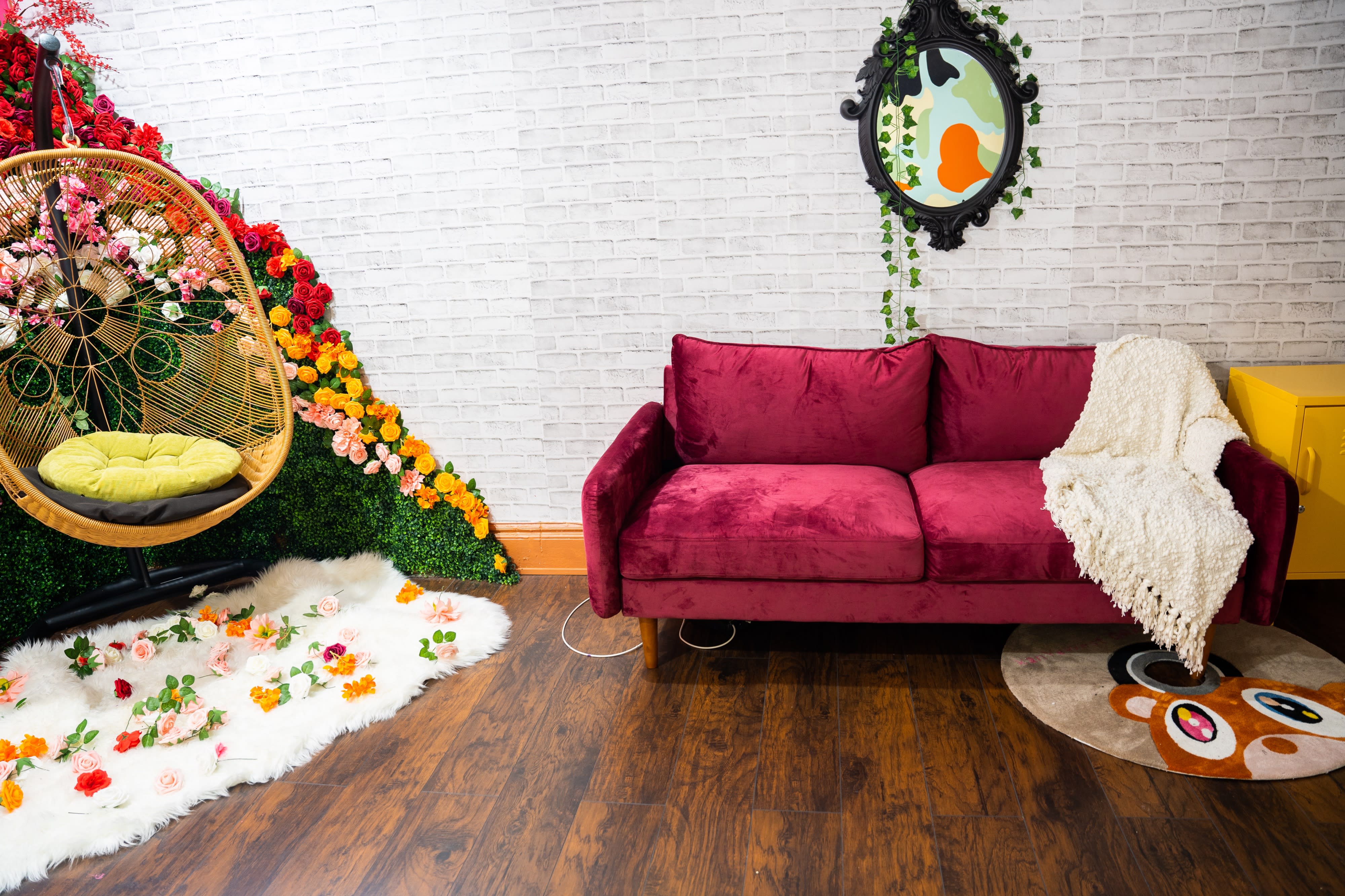 A woman in a yellow dress sits in a wicker chair surrounded by an arrangement of colorful flowers and greenery.