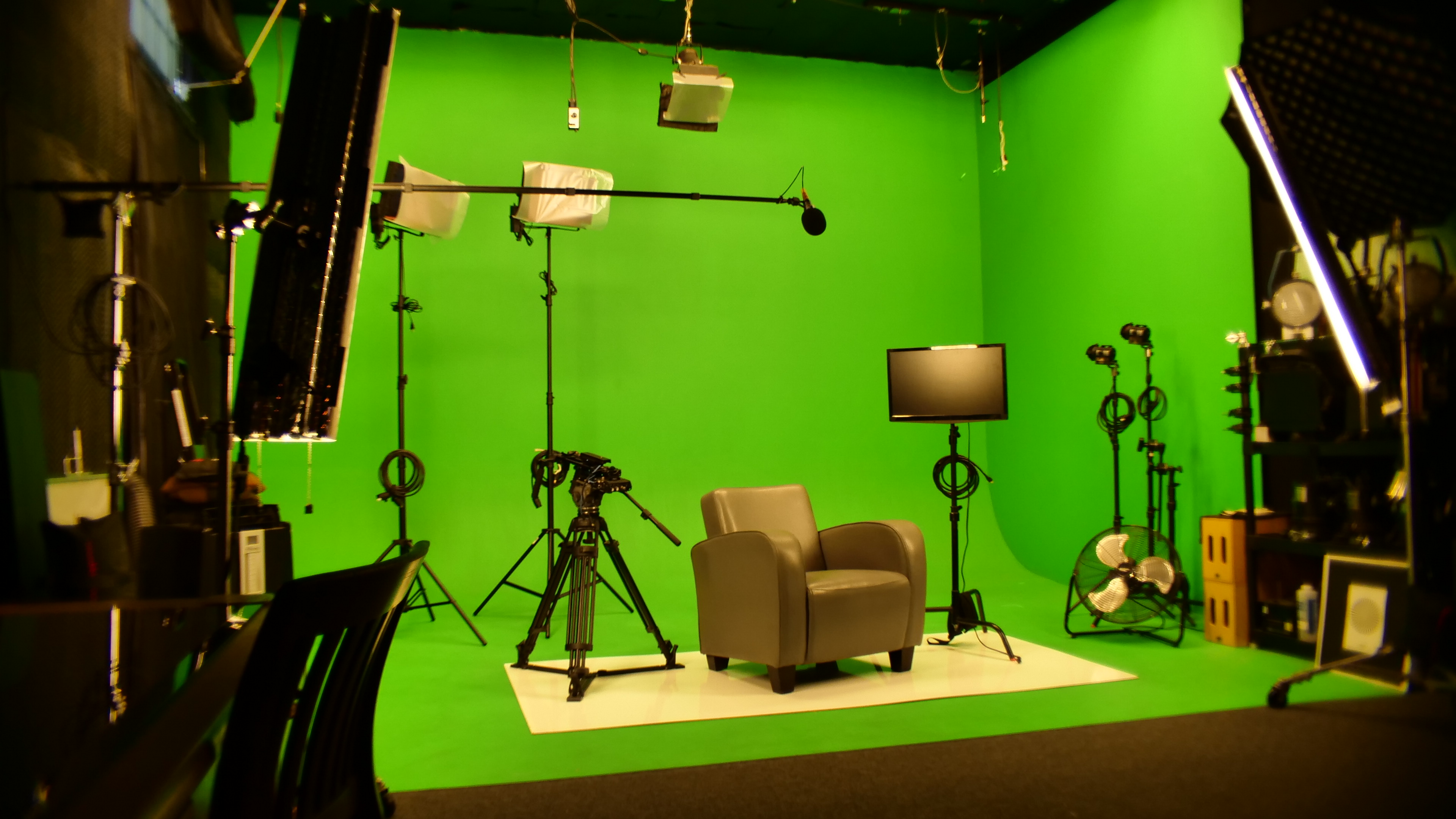 A person lies on the green screen floor of a video shoot, surrounded by filming equipment and lighting.