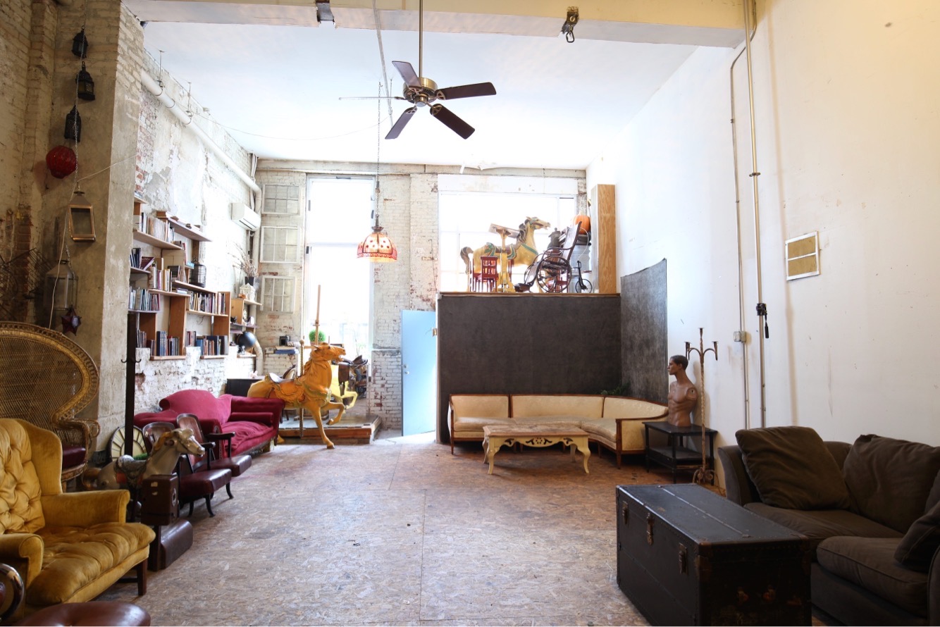 The scene shows a vintage-style room with eclectic furniture, including an armchair and a couch, as people mingle and socialize in the background.