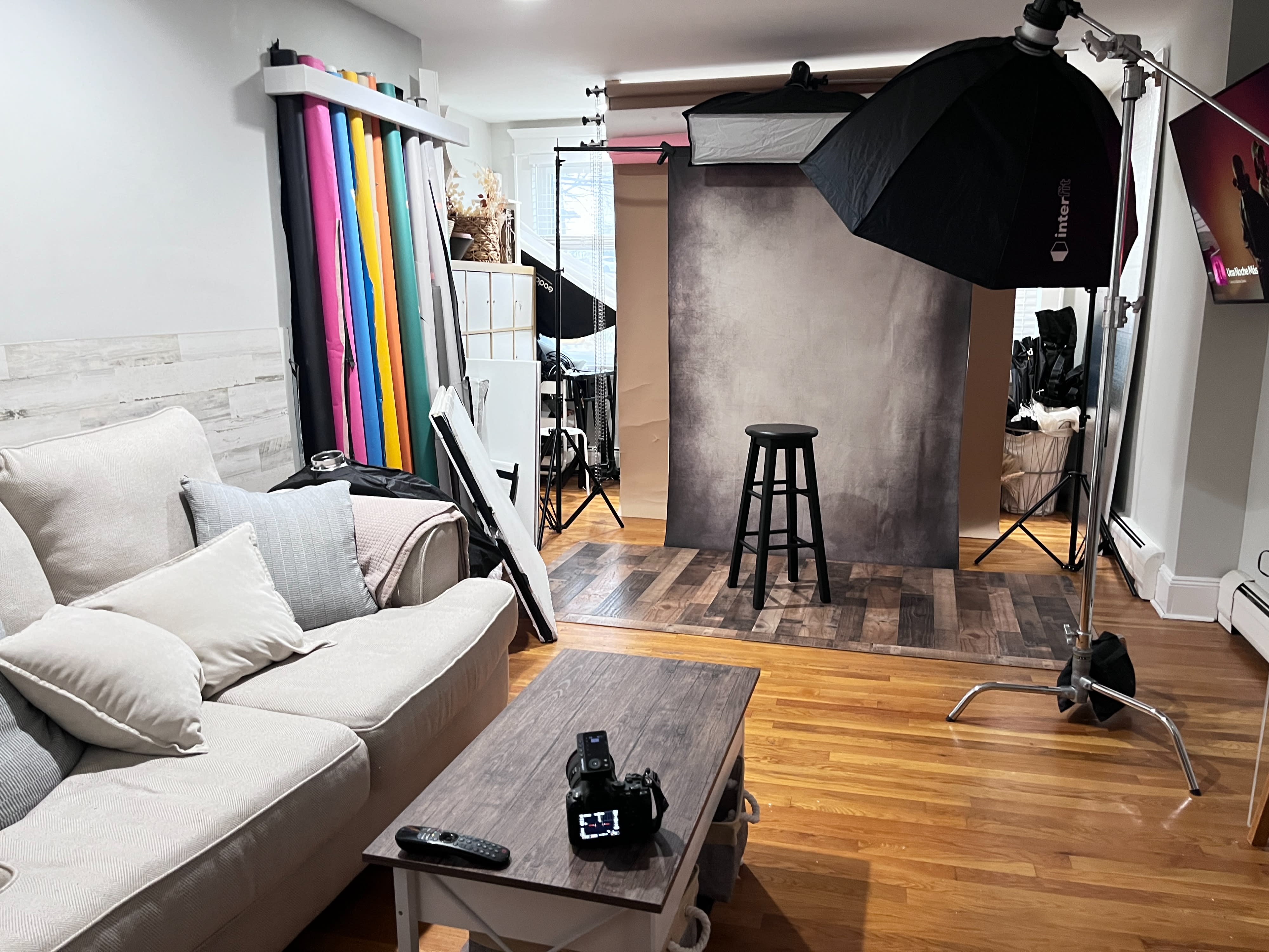 A woman in activewear is posing with her arms extended while sitting on a stool during a video shoot.