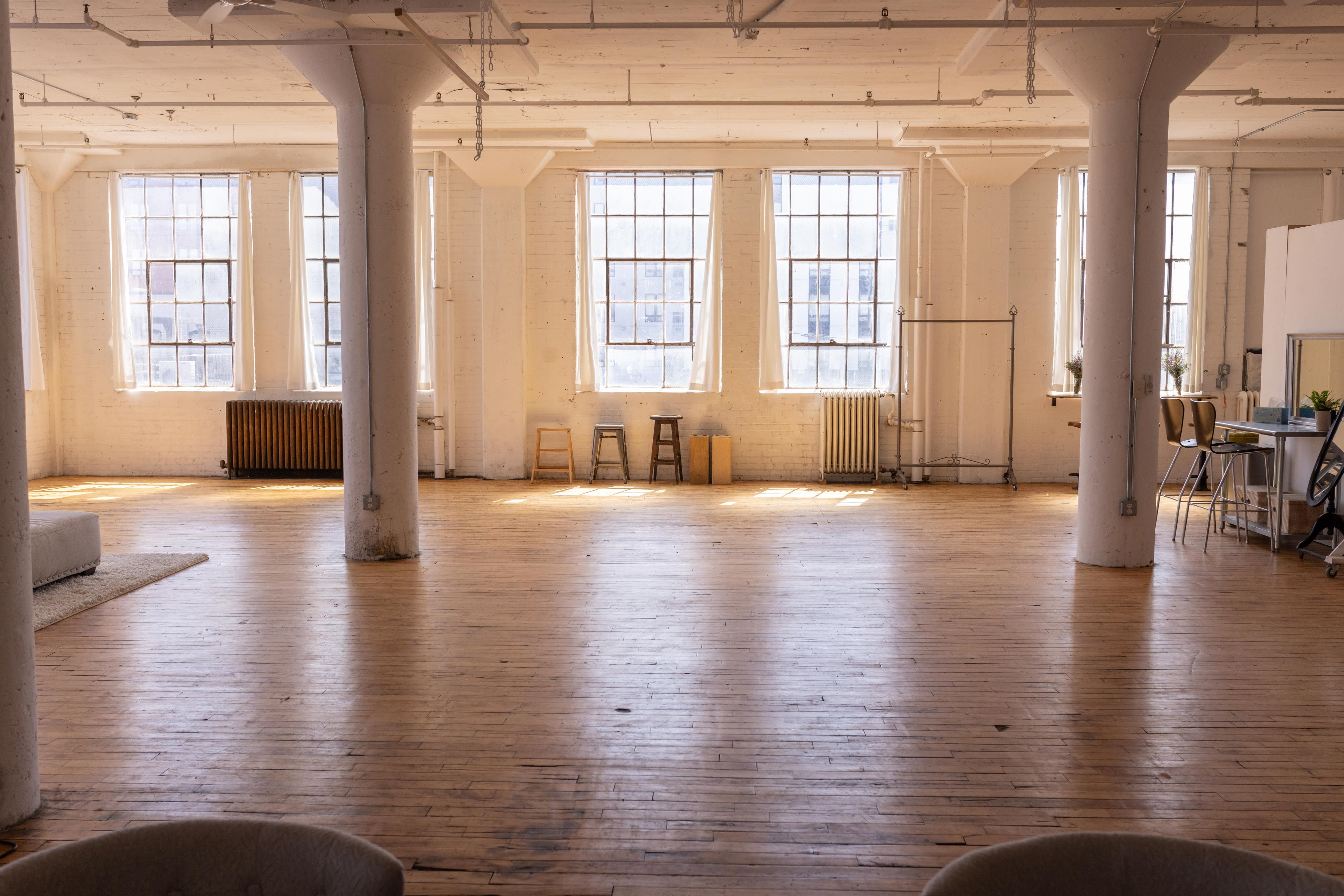 A photographer sets up a white backdrop in a well-lit studio with large windows.