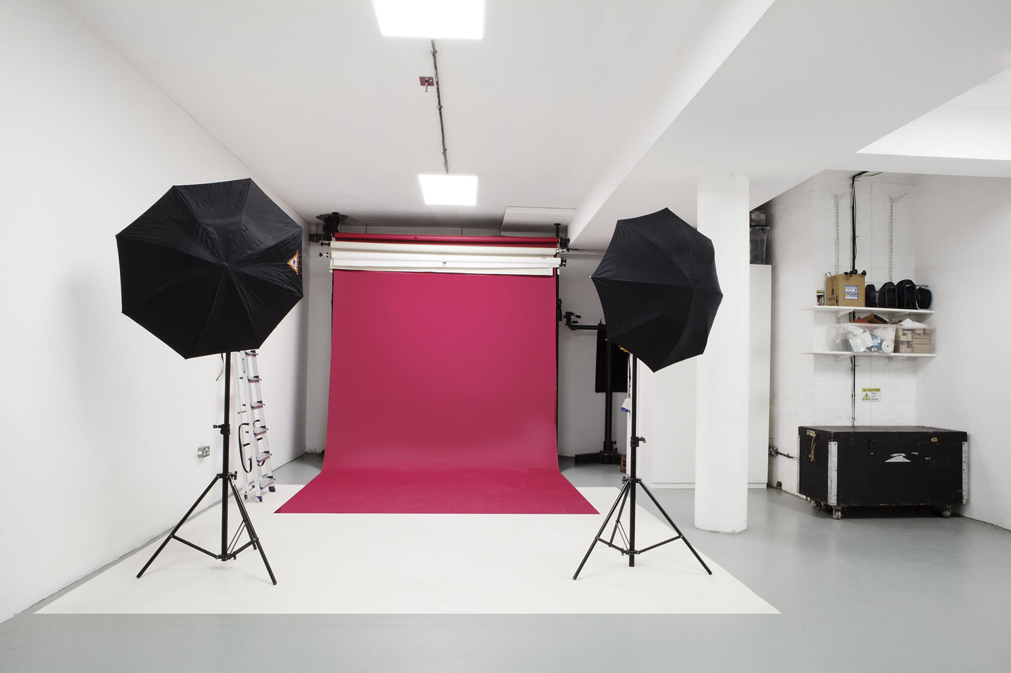 A film crew conducts a green screen shoot with one person on a stool while others manage equipment and review scripts.