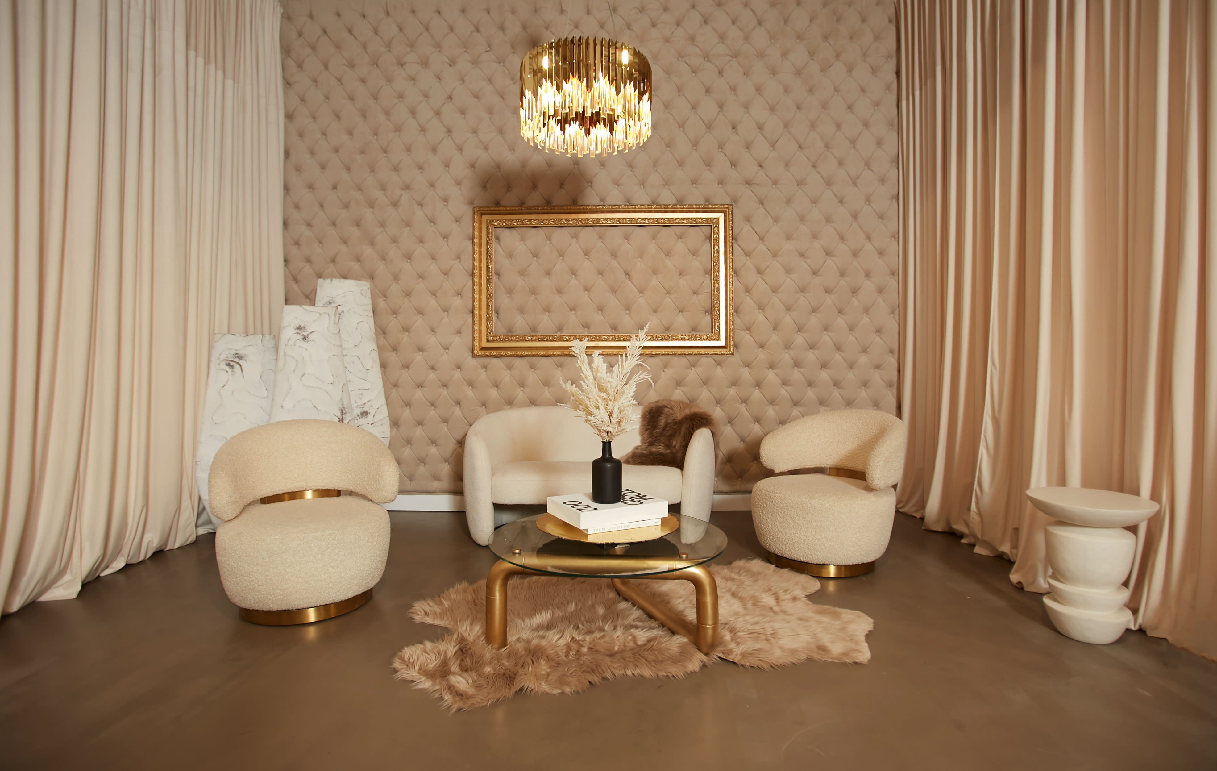 A group of eight women poses together in a stylish photo shoot setting with a decorative backdrop and elegant furnishings.