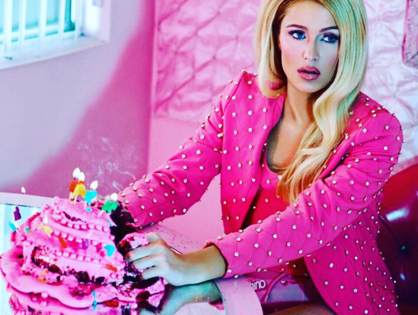 A model poses in a pink-themed room, twirling her sheer dress amidst vibrant decor.
