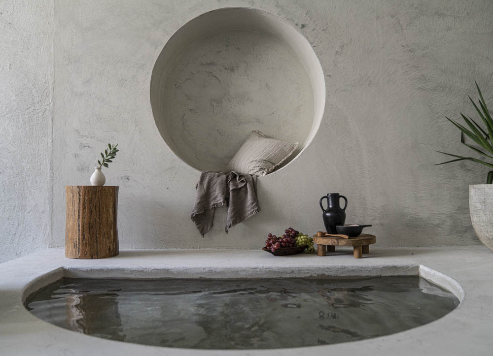 A woman poses in a circular alcove, cradling her belly and seated comfortably against the wall, surrounded by decorative items.