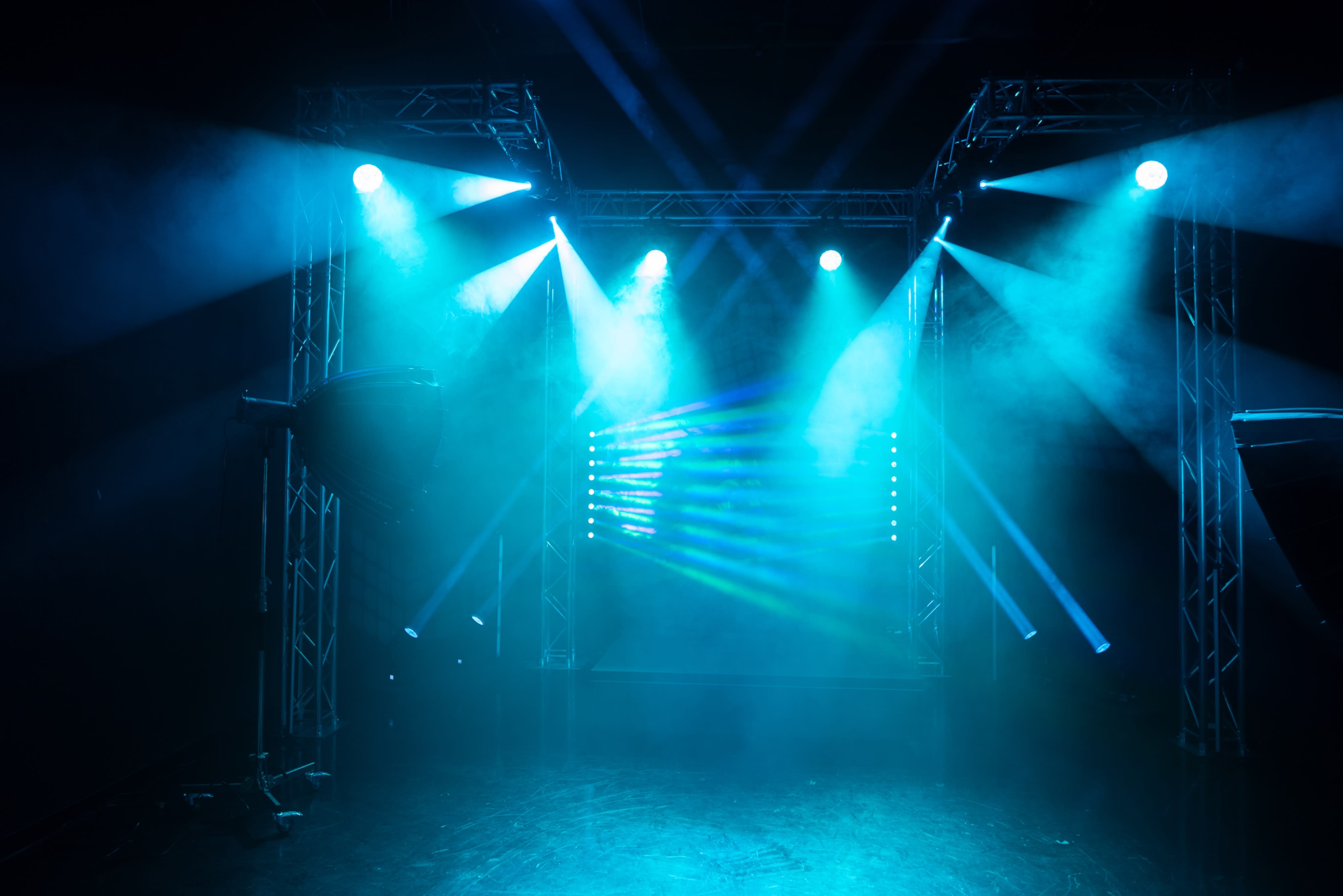 A figure stands in a foggy setting, illuminated by two bright lights from above, emphasizing a moment of anticipation before a performance.