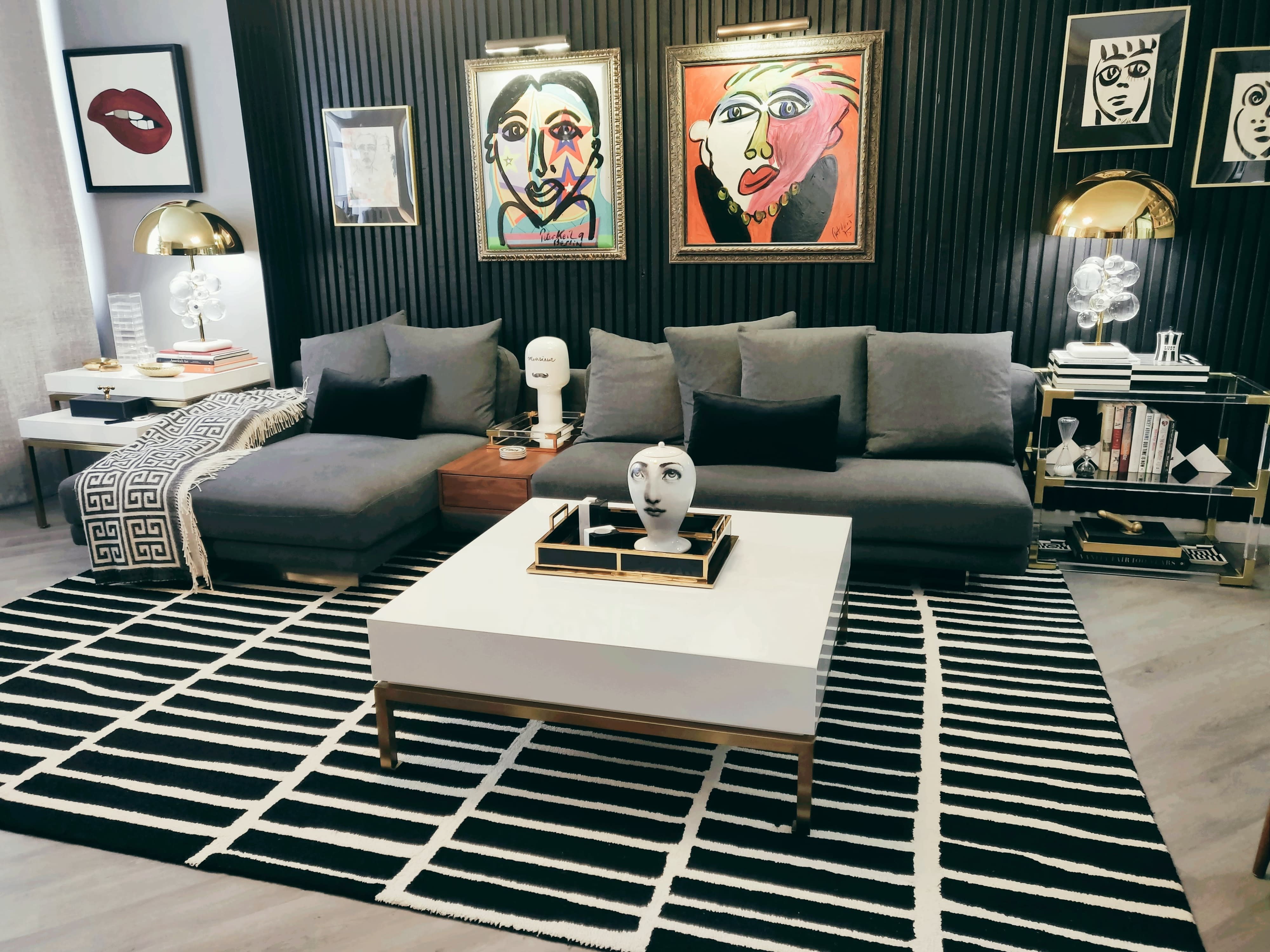 Two women pose for a magazine photo shoot on a modern sofa in front of vibrant artwork.
