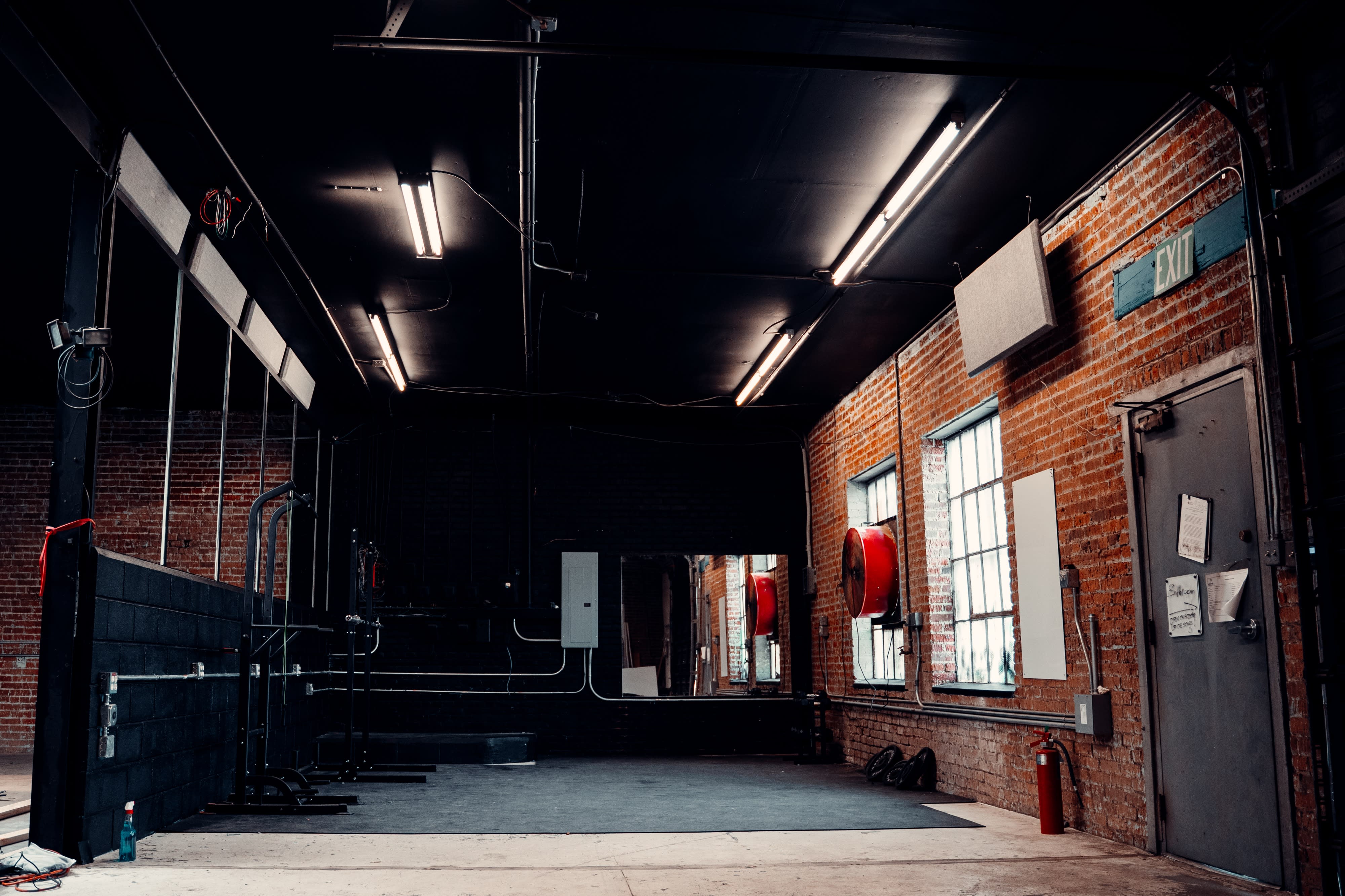 A person is performing a handstand in an industrial space with yellow support beams and a shaft of light illuminating the floor.