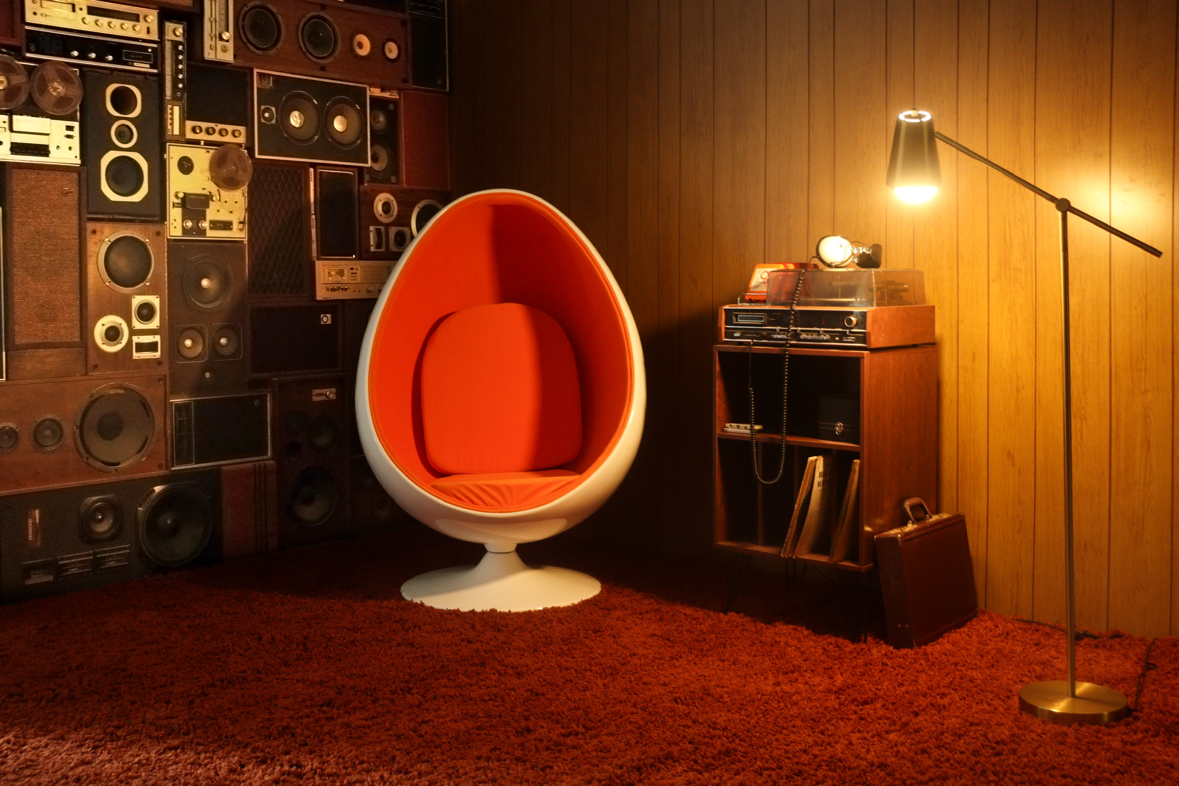A person sits in an iconic round chair against a backdrop of vintage speakers while looking down.