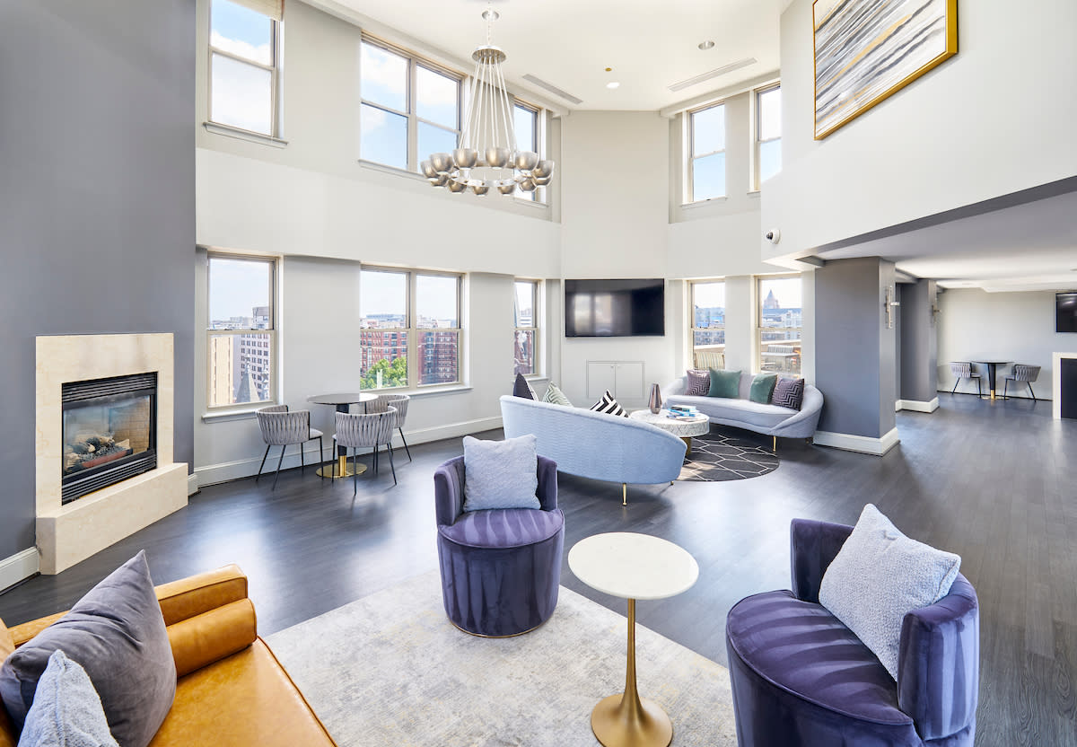 The spacious living room features a modern sofa, a round coffee table, and a small dining area near the windows, all illuminated by the city lights outside.