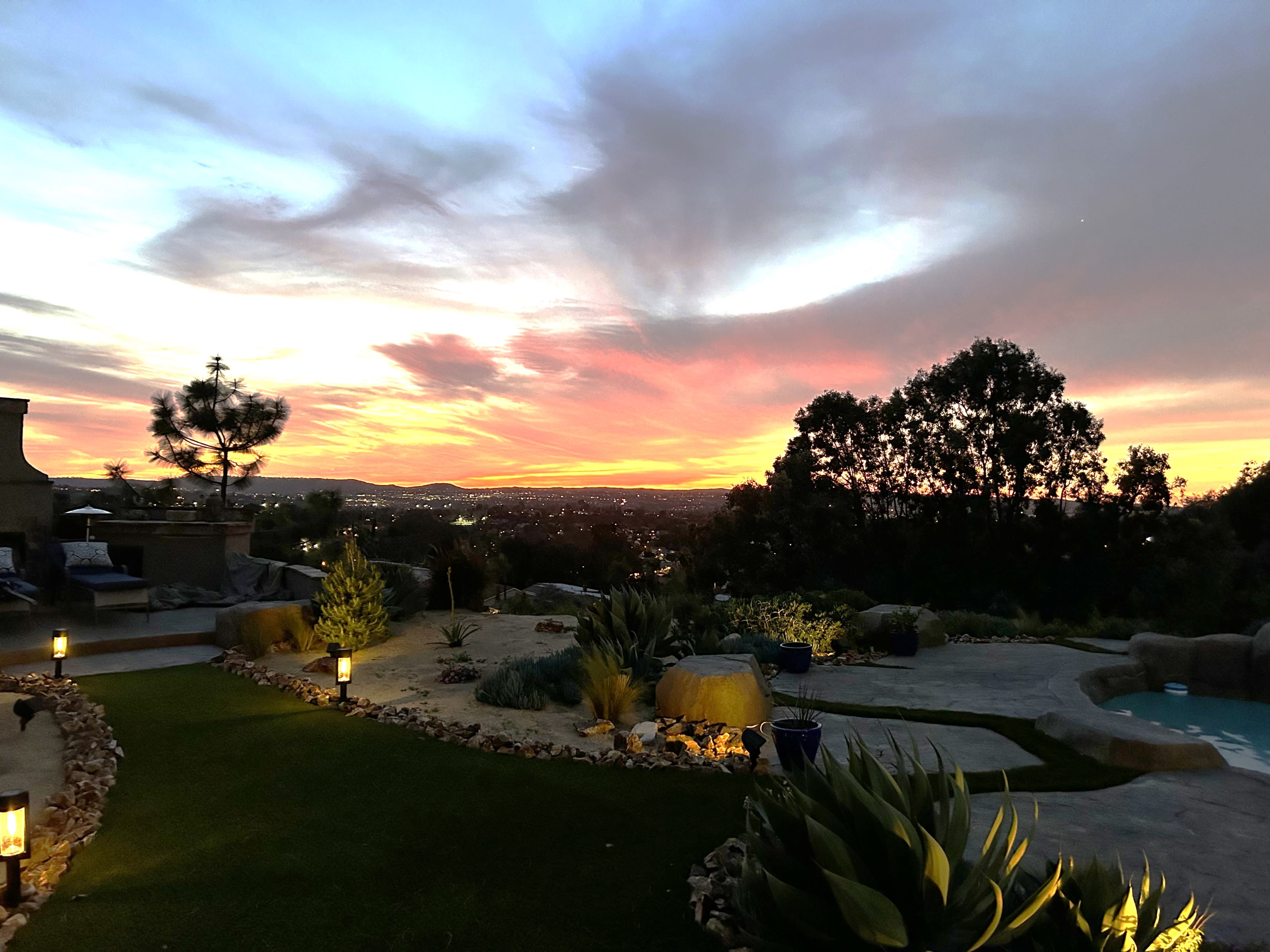 A cozy outdoor birthday dinner is set by a fireplace, with a view of twinkling city lights and an array of empty wine bottles on the counter.