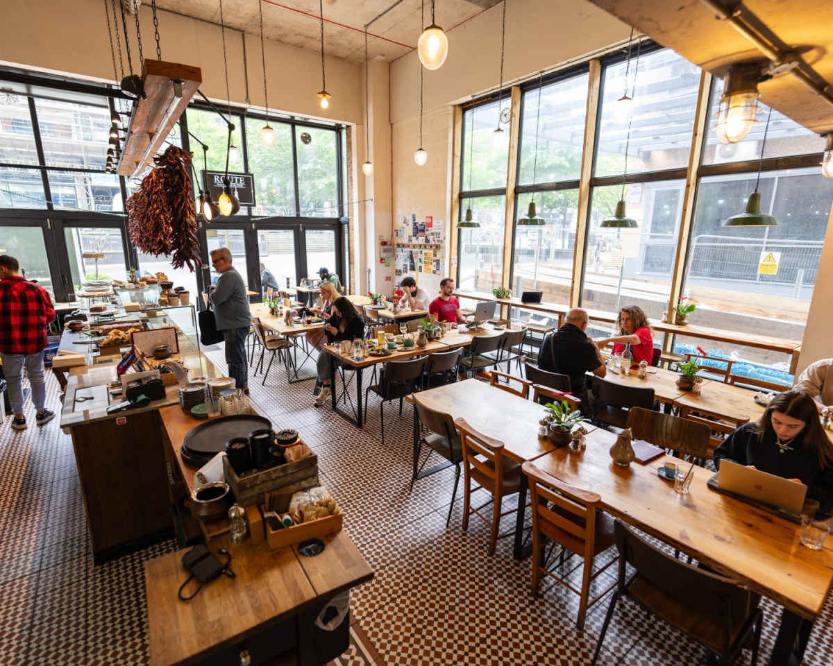 A beautifully arranged dining table with floral centerpieces sits in a cozy restaurant setting, while a chef prepares food in the background.