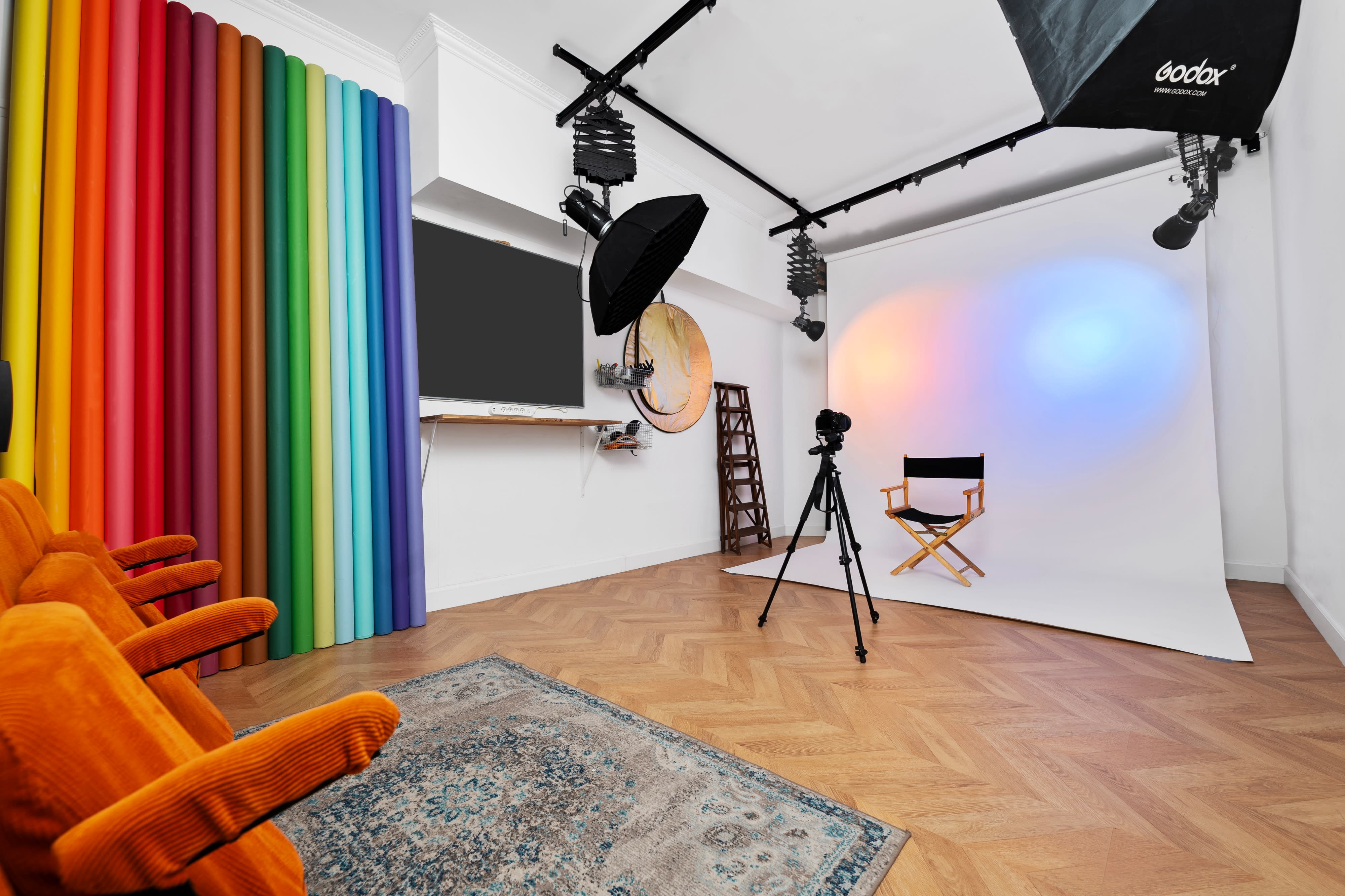 The image shows a photo studio setup, featuring a photographer with a model standing on a backdrop, multiple lighting rigs, and equipment laid out on a table.