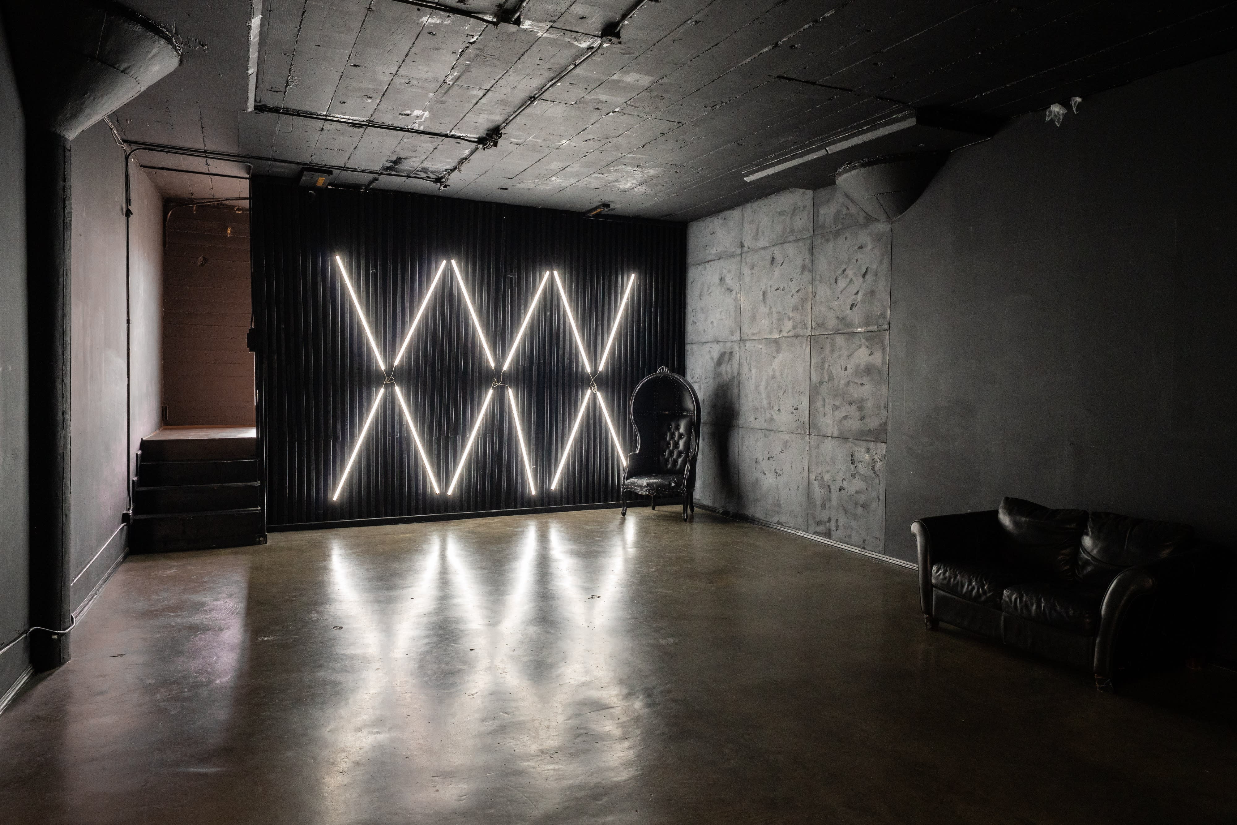 A videographer records a drummer performing in a dimly lit studio with geometric lighting.