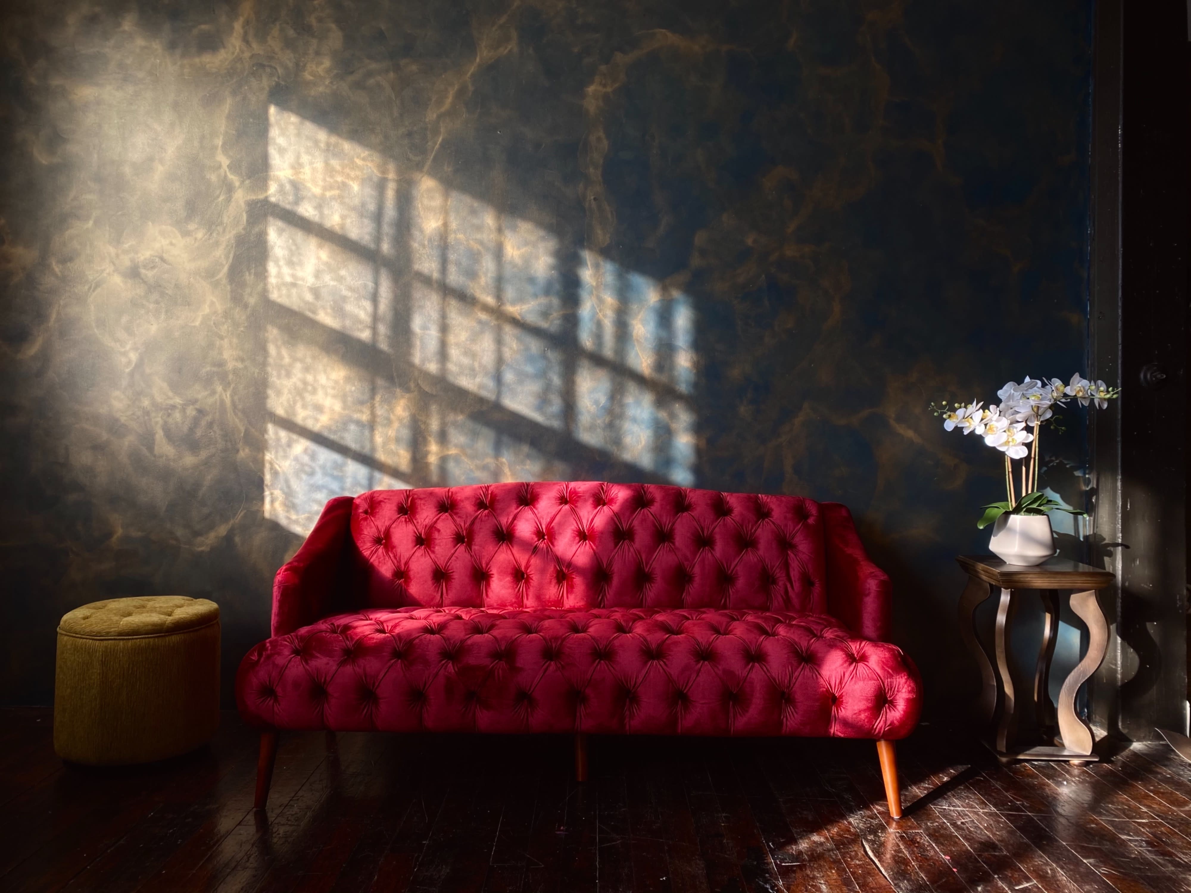 A model poses on a dark fur rug in a red lingerie set, leaning on one arm in front of a pink couch.