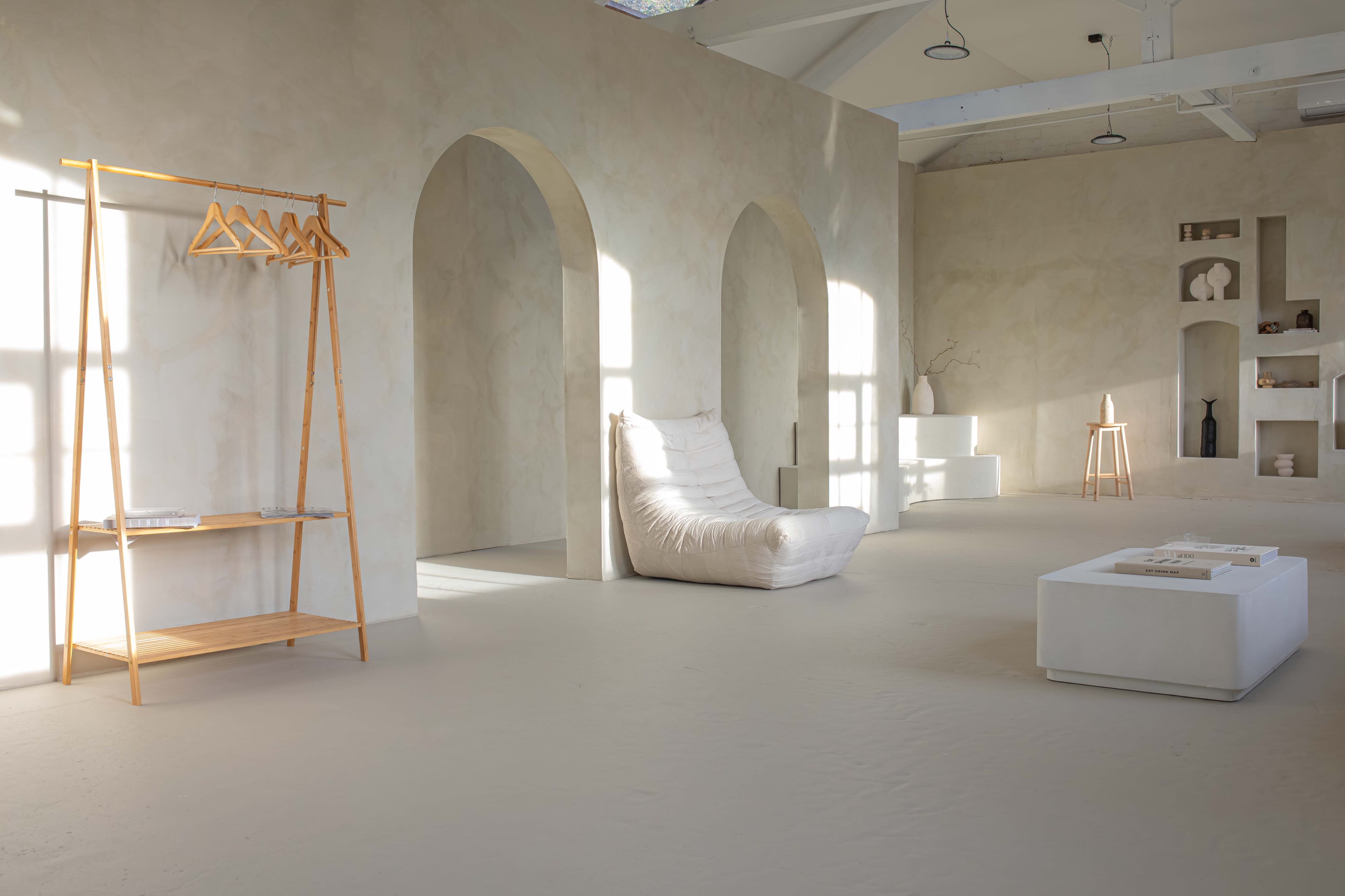 The scene features a minimalist interview setup with smooth, curved seating, a decorative vase, and a large mirror against a softly textured wall.