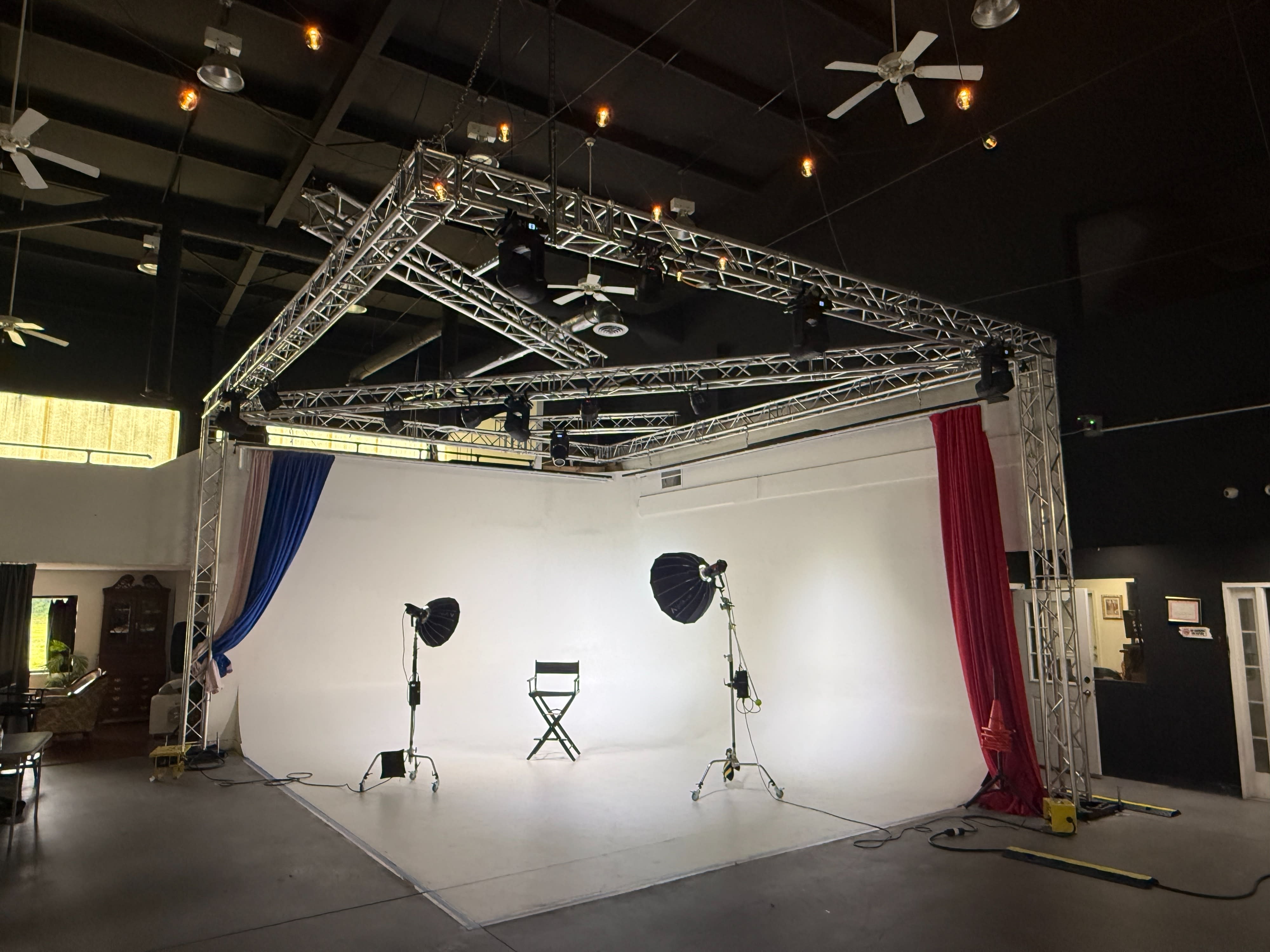 A film crew is preparing for a video shoot in a studio, with one person adjusting the camera while two others discuss the setup.