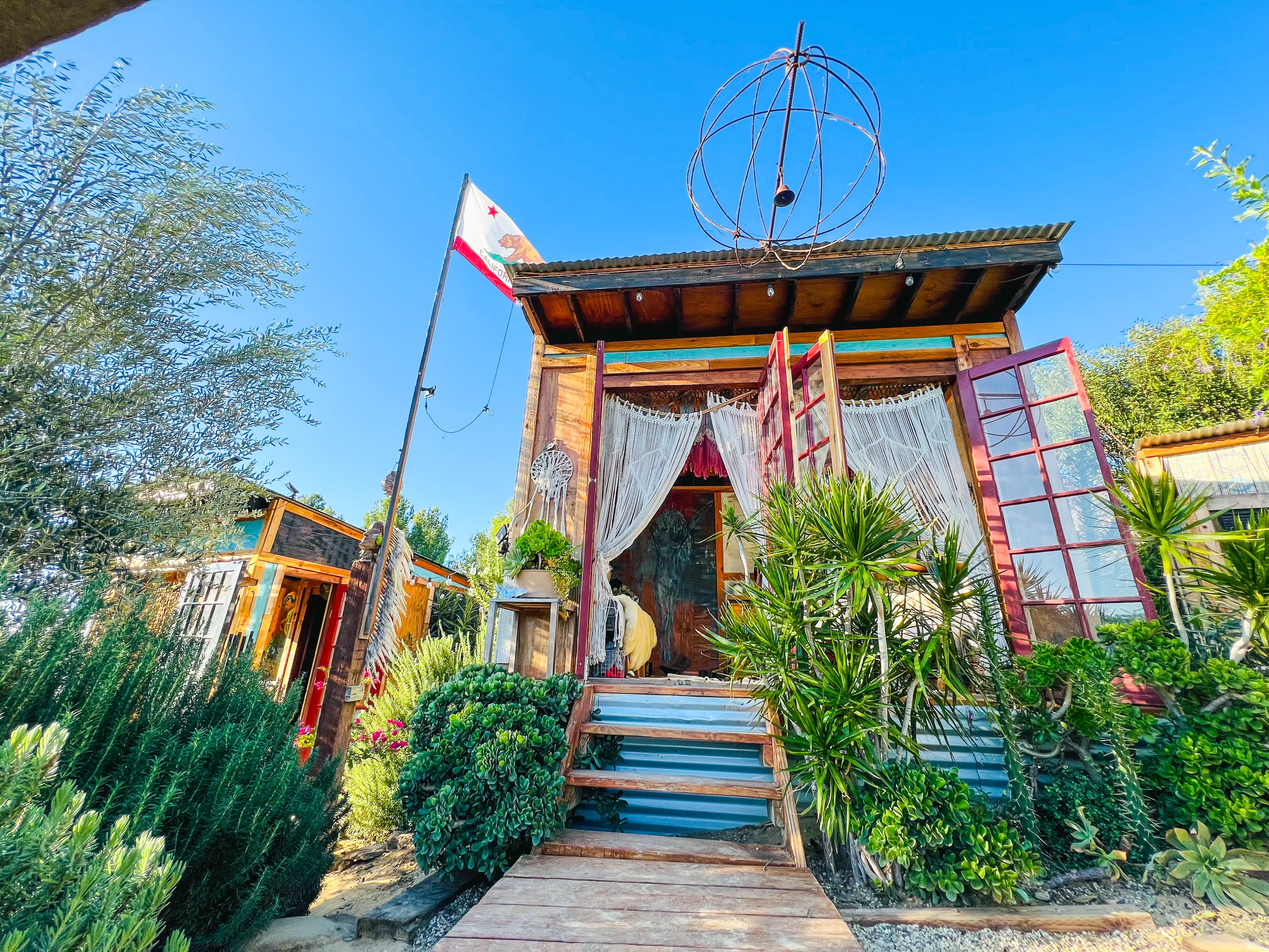 A cozy interior with a bed draped in a fur blanket and macramé curtains, viewed through red-framed glass doors.