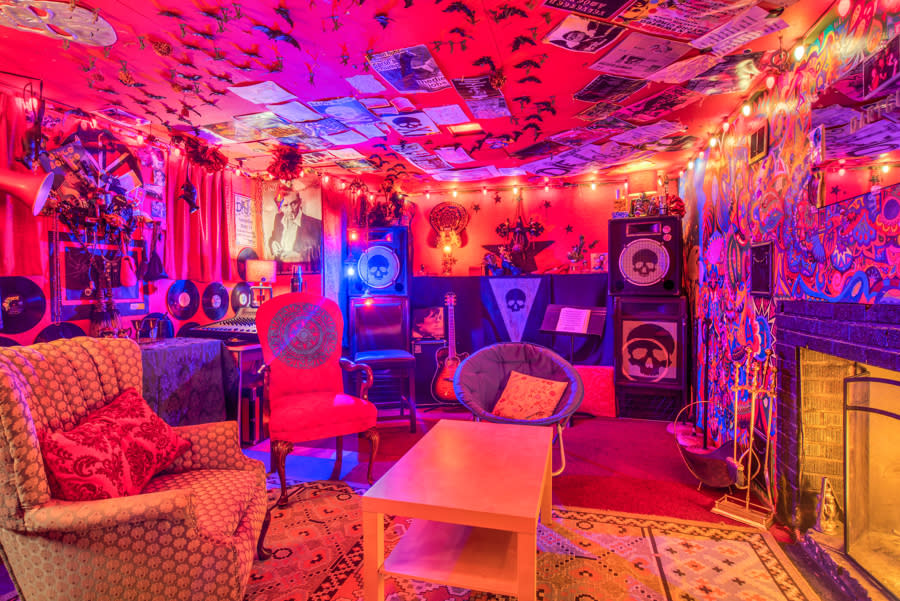 Two women in colorful chairs sit in a cozy, dimly lit room decorated with posters and string lights, engaging in conversation at a graduation party.