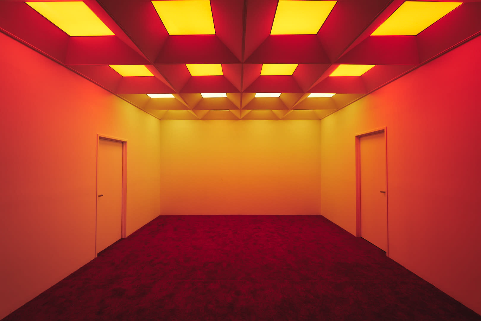 A model poses on a red carpet in a geometric room with a stark shadow against the wall.