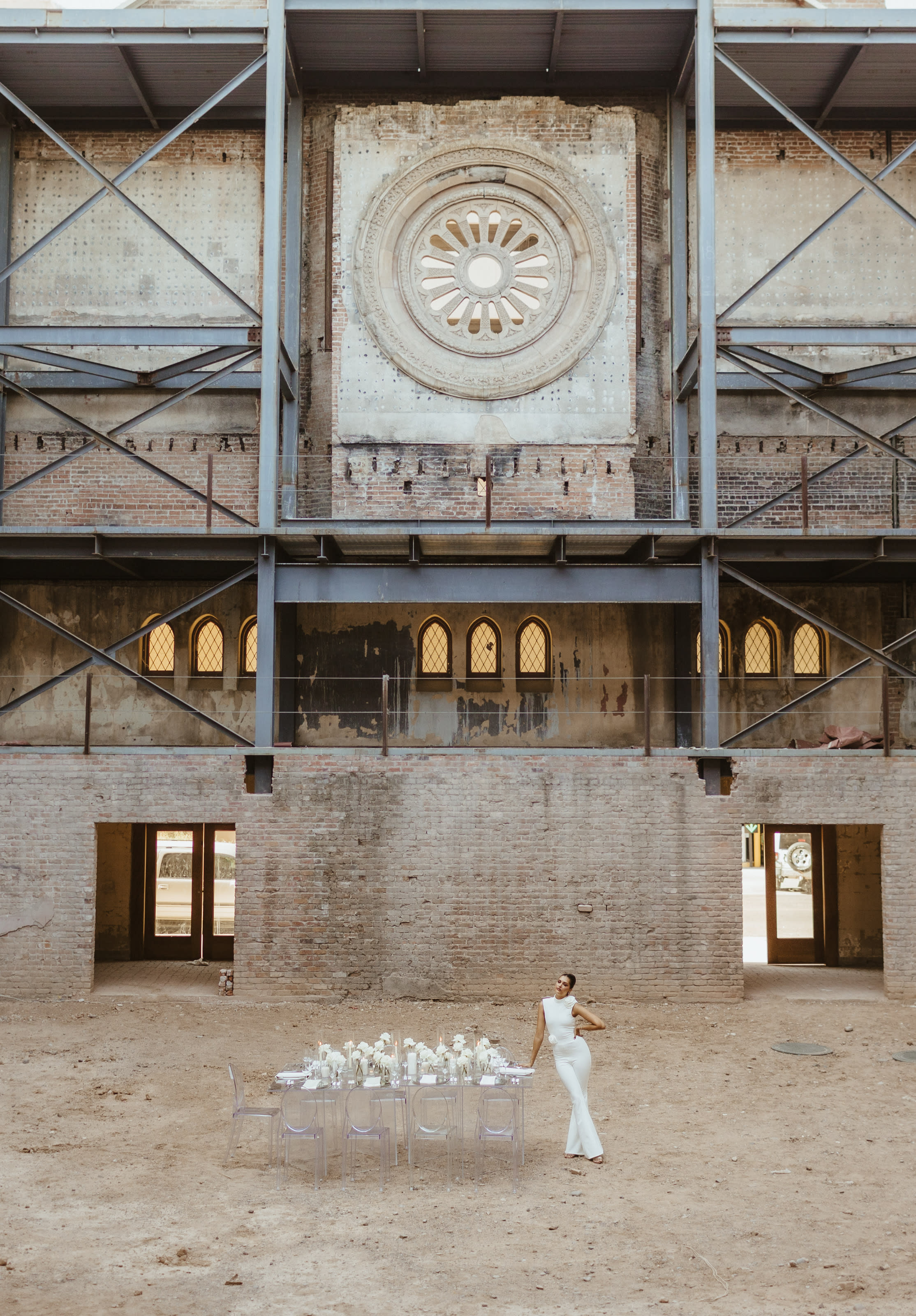 A couple poses together in a bridal photo shoot against a backdrop of industrial architecture.