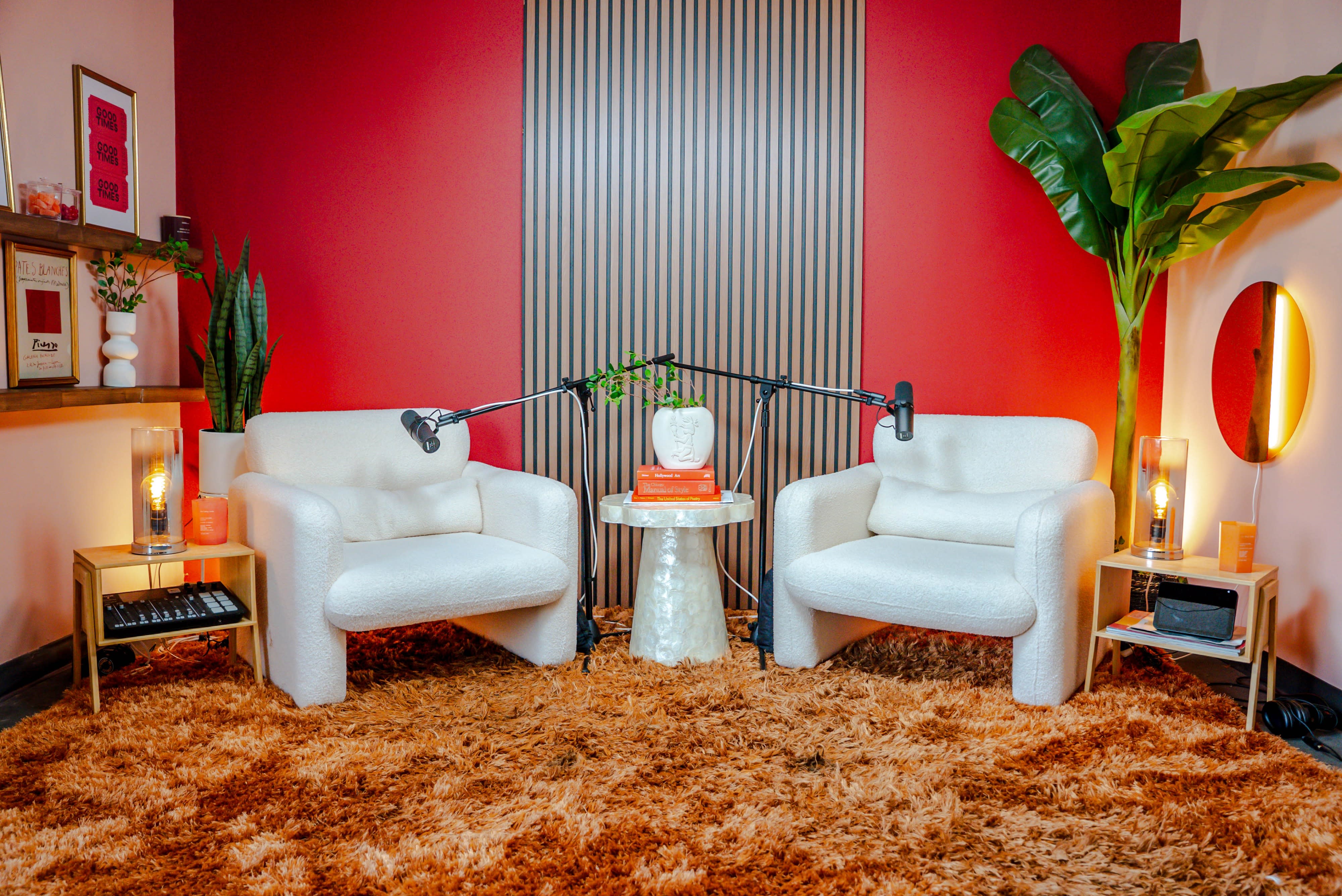 Two individuals are seated in cozy armchairs, engaging in a podcast recording session with microphones positioned in front of them.