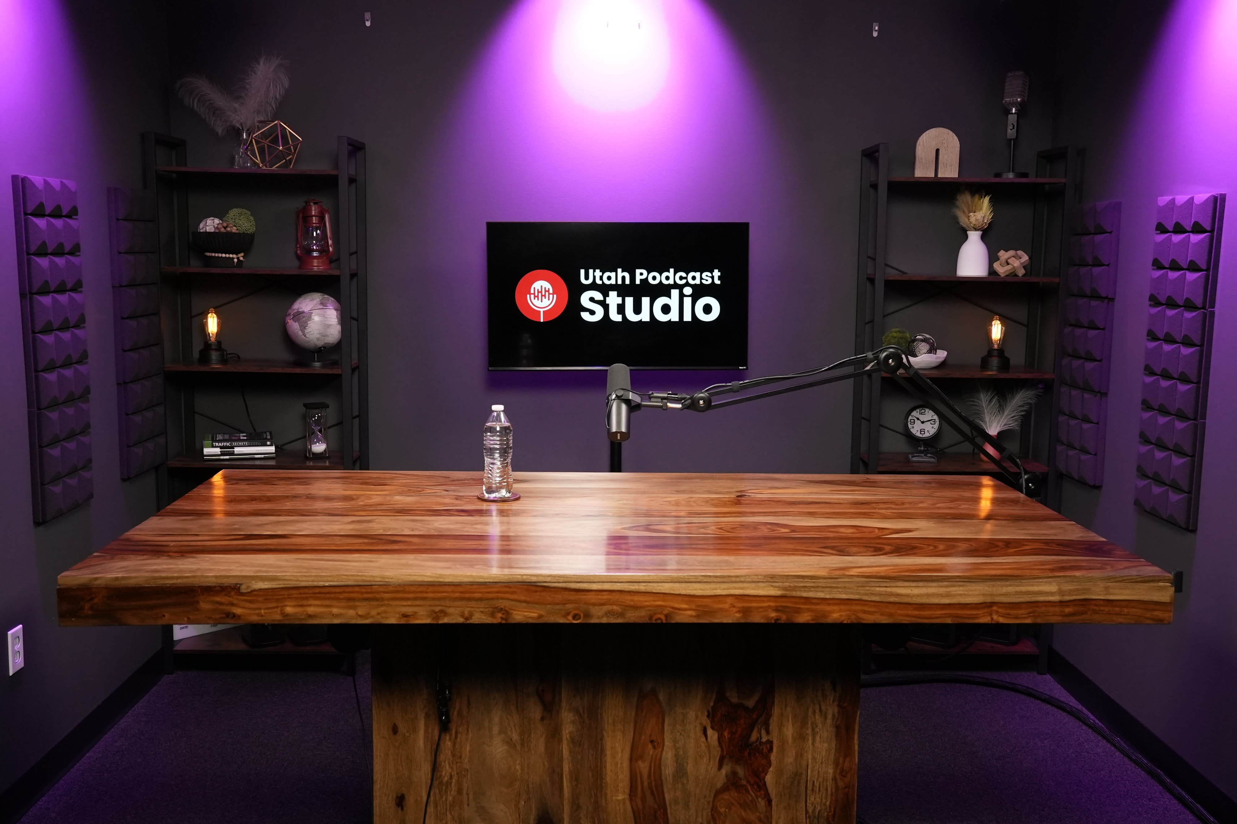 Two individuals sit across from each other at a wooden table, engaged in a conversation for a podcast recording, with microphones positioned in front of them.