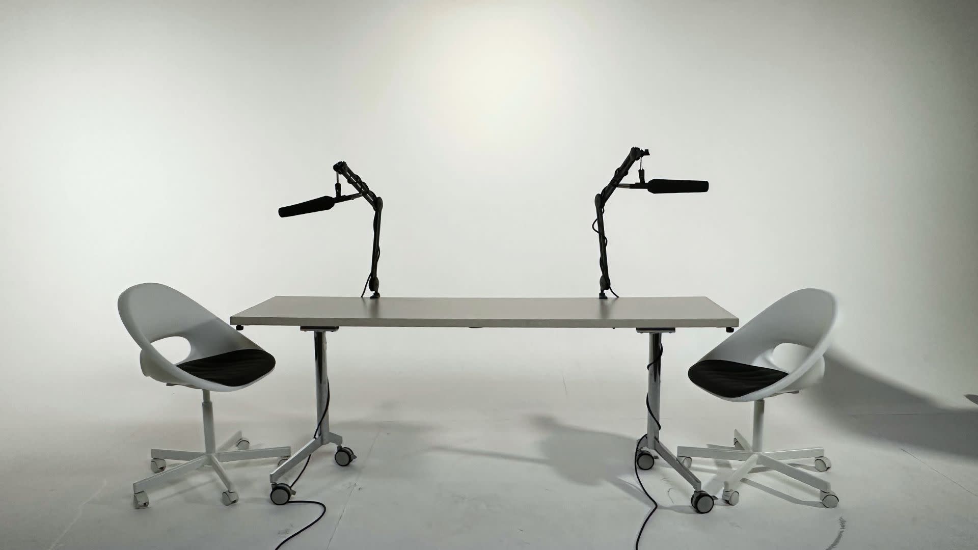 A musician plays a keyboard while seated in front of a microphone in a studio with blue lighting.